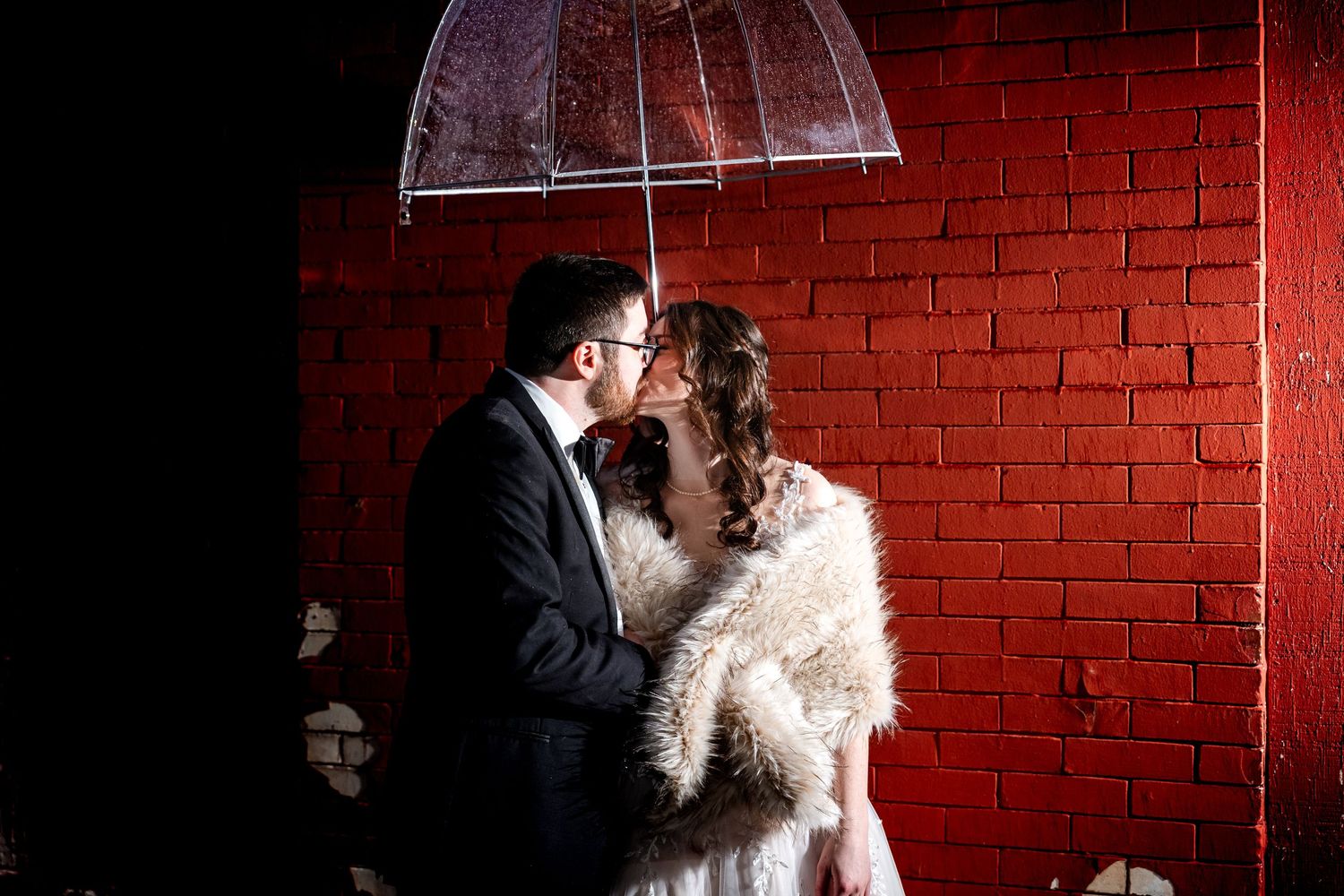 Dramatic portrait against red brick wall with moody lighting.