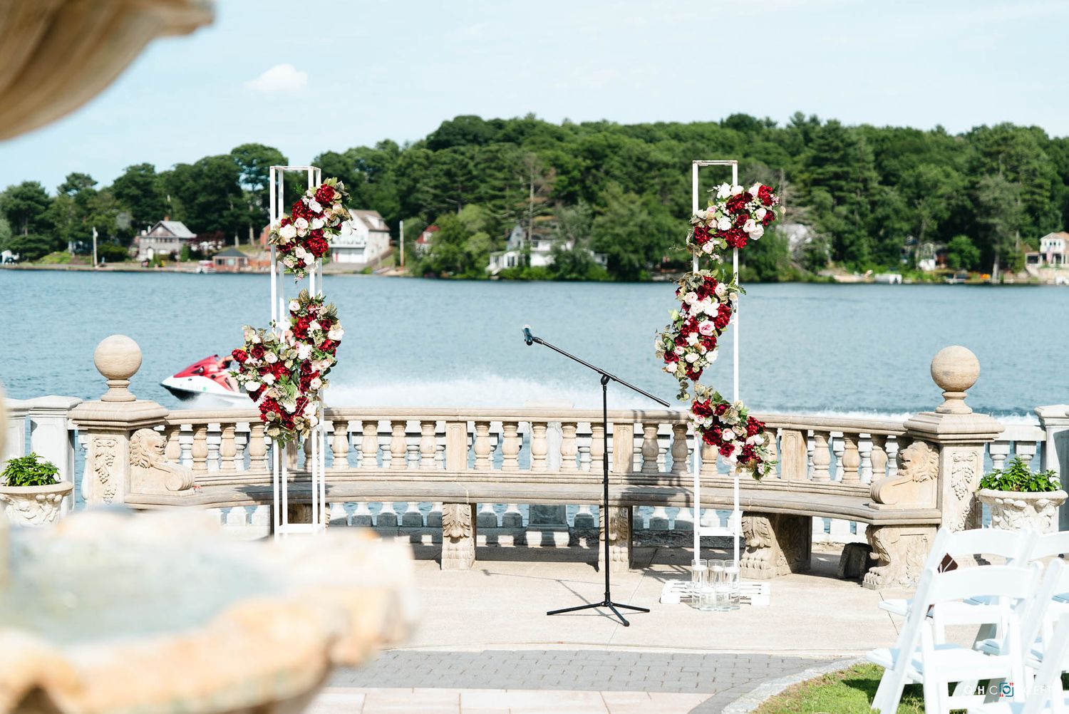 Outdoor wedding ceremony setup with floral arch decorations overlooking a scenic lake and waterfront homes.