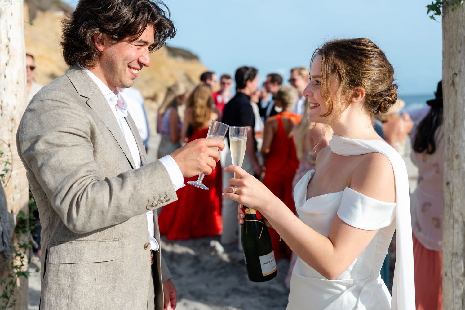 Wedding celebration on the beach with guests enjoying the ceremony under blue skies.