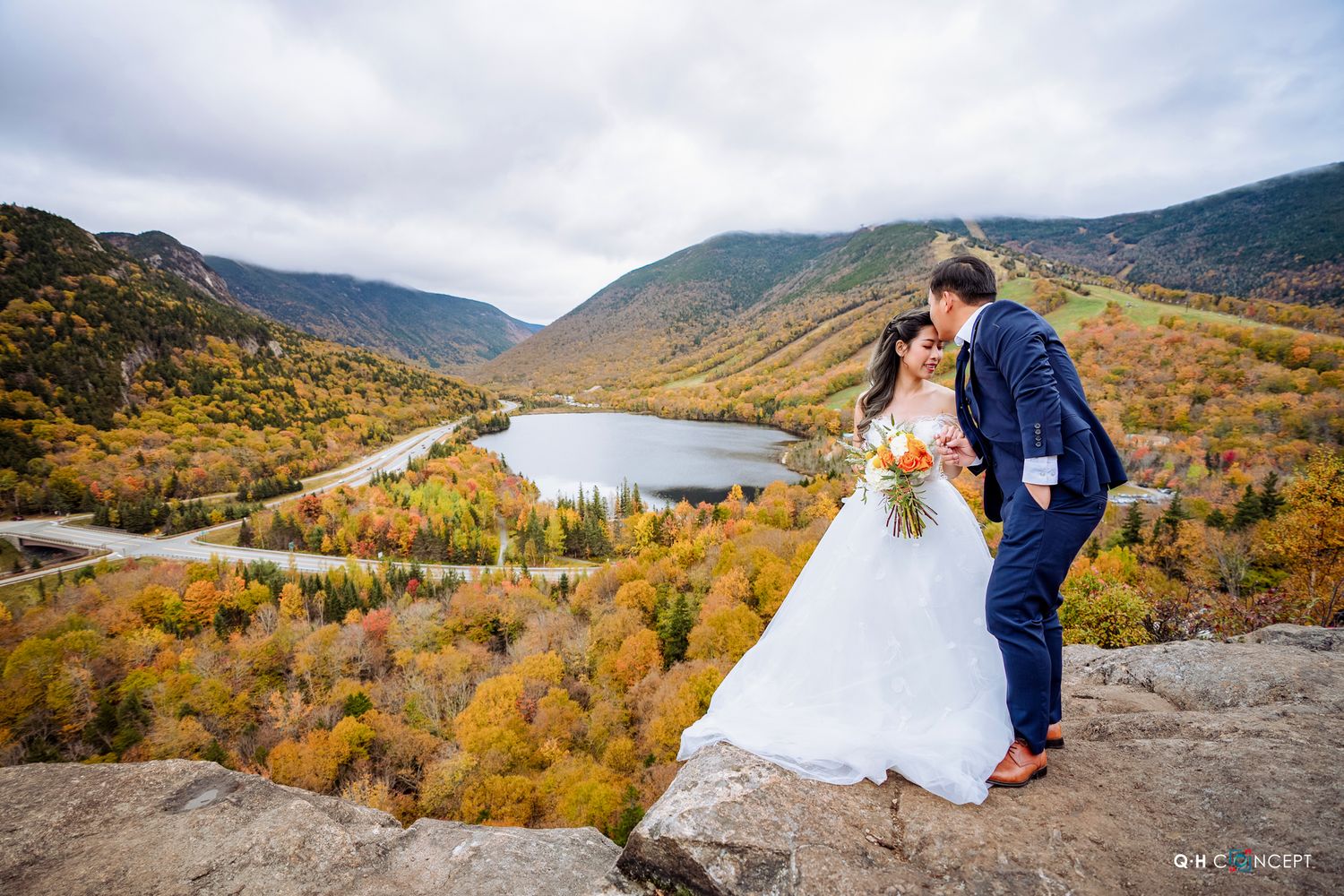 A scenic mountain overlook with vibrant fall foliage and dramatic cloudy skies.