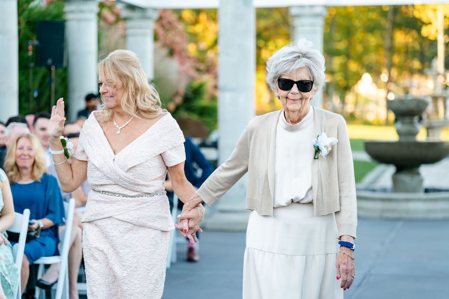 Two women in white outfits walking together during outdoor wedding ceremony.