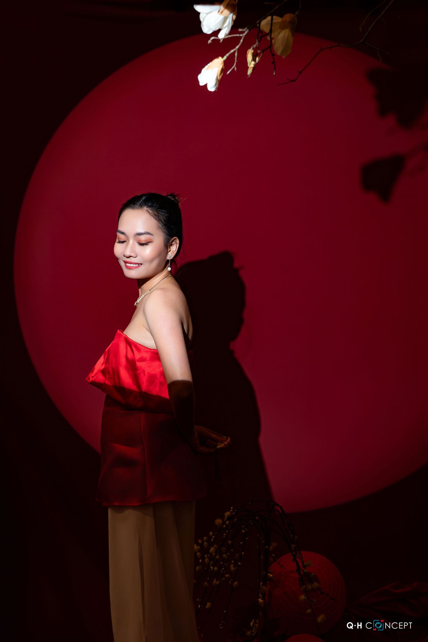 A woman in a red dress poses against a dark background with dramatic lighting and shadows.