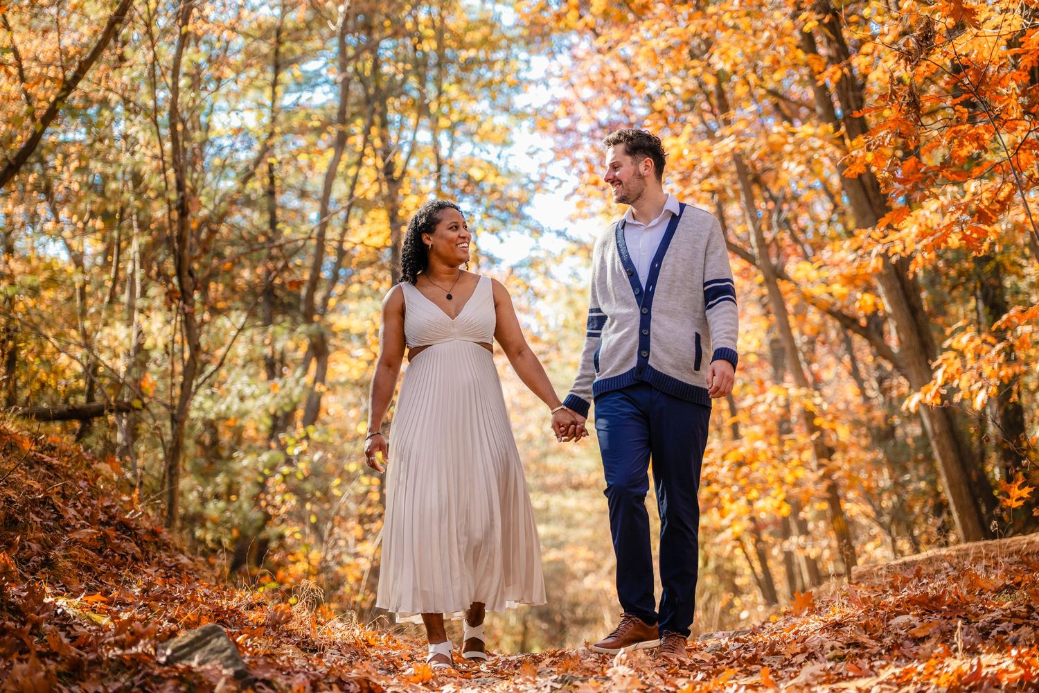 Couple walking hand in hand through a forest path with vibrant fall foliage.