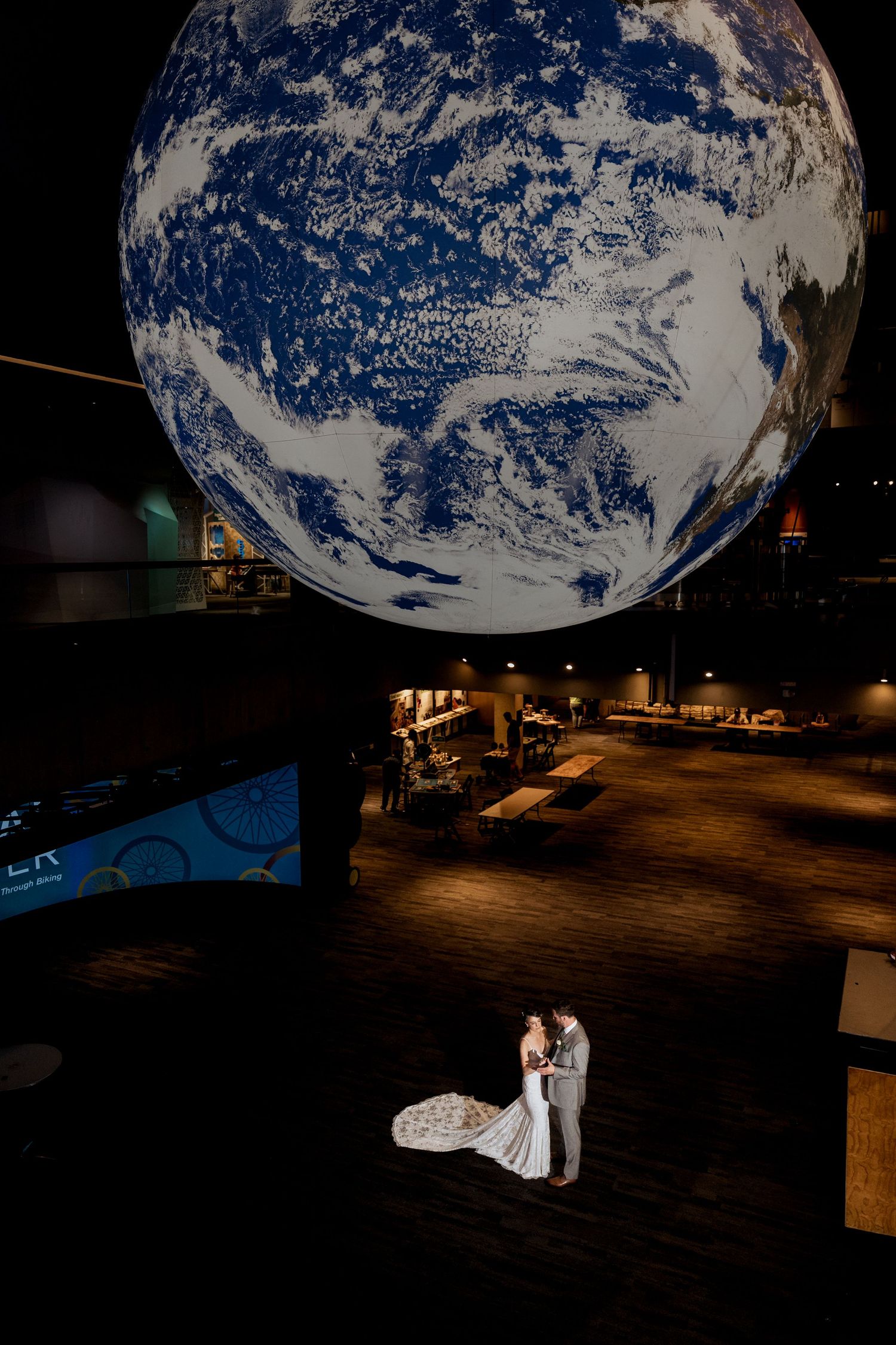 A couple shares an intimate moment beneath a large illuminated Earth globe display in a dark exhibition space.