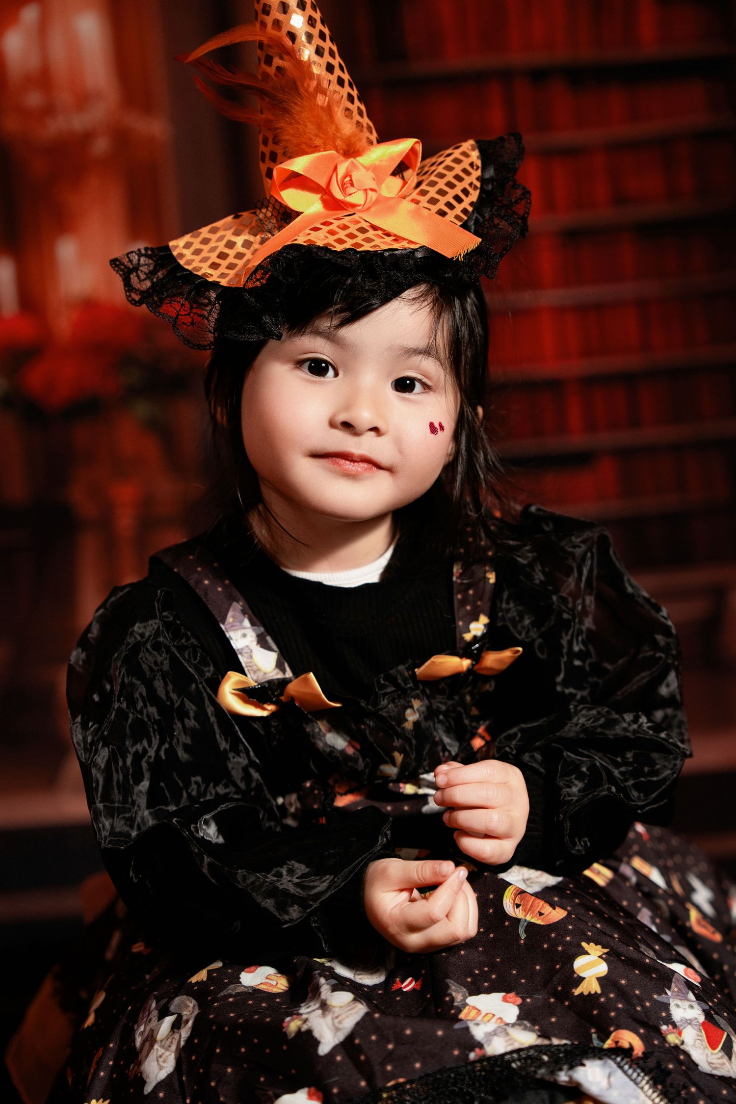 Festive portrait in black dress and orange witch hat against library backdrop.