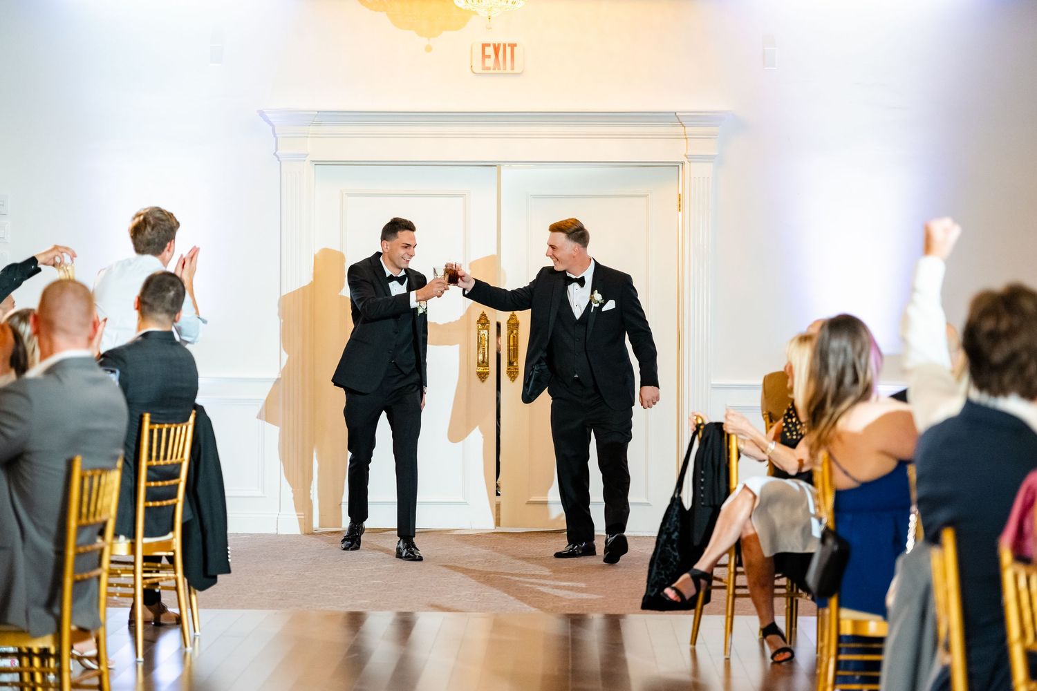 Wedding party members perform choreographed dance moves in a bright ballroom venue.