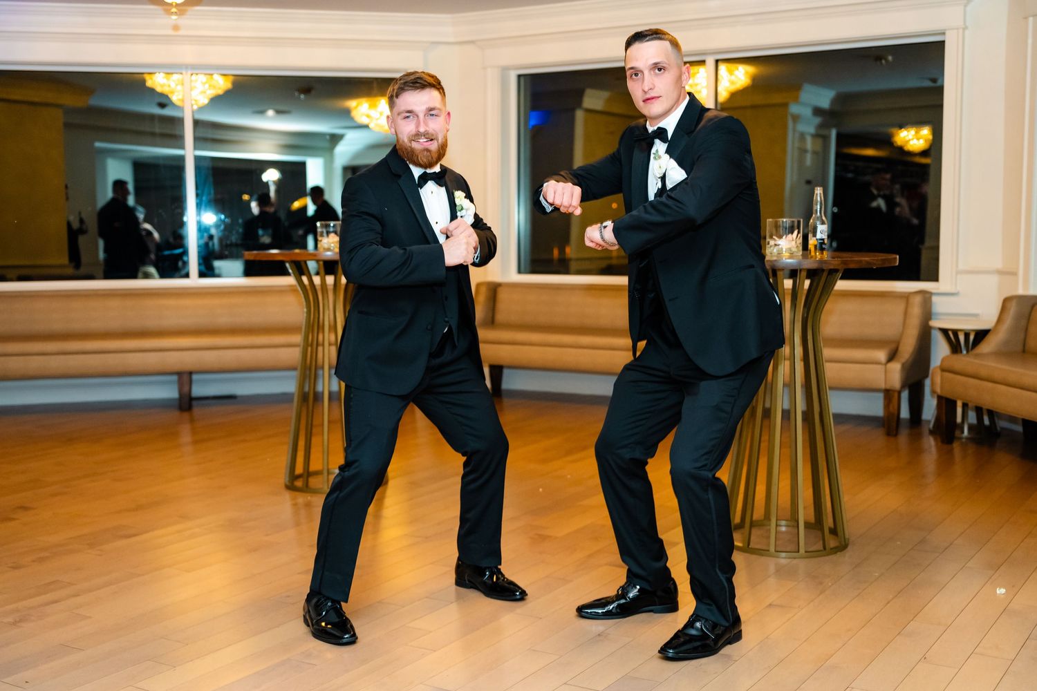 Men in formal attire strike fun poses on the dance floor at a wedding reception.