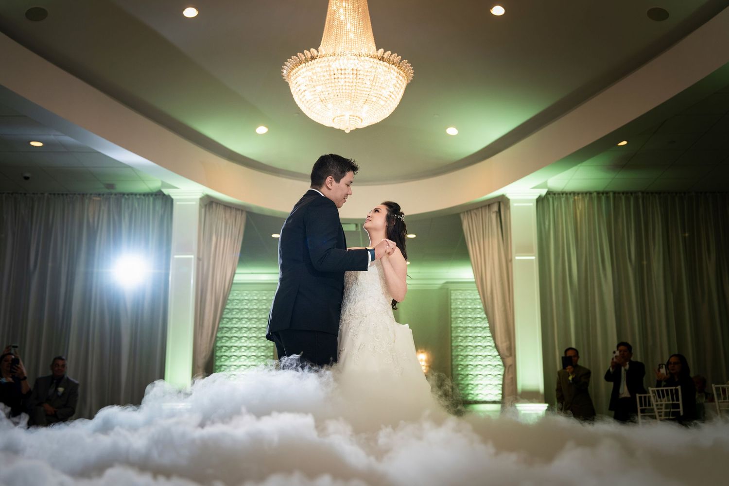 Wedding reception in elegant ballroom with crystal chandelier and mood lighting.