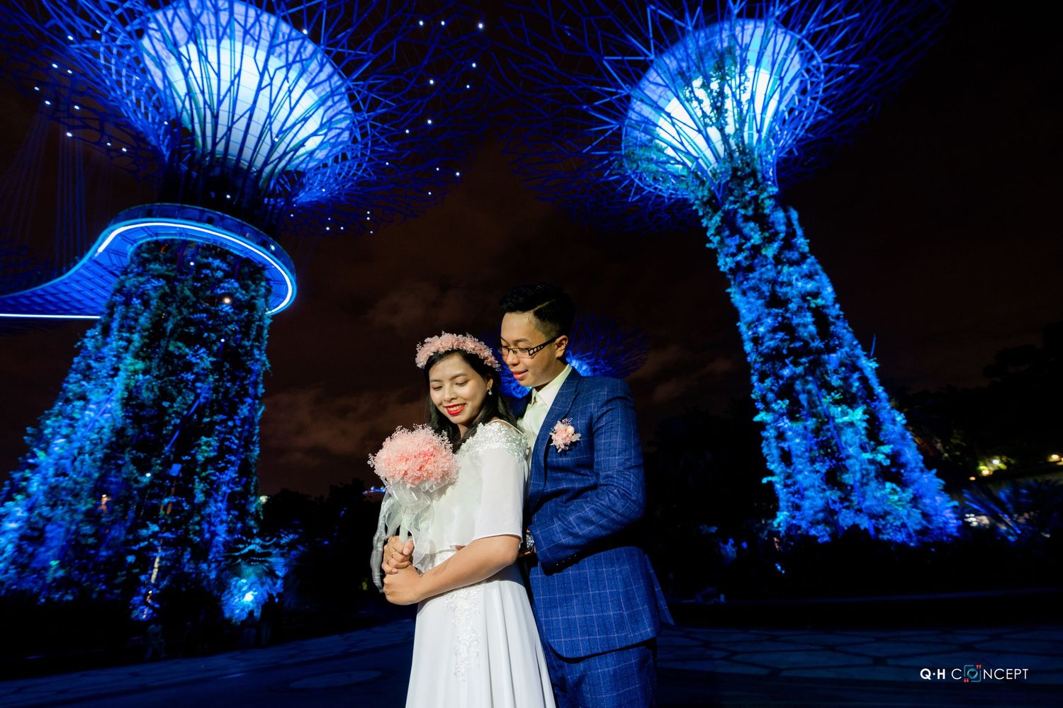 Wedding couple shares romantic moments under illuminated blue trees at night.