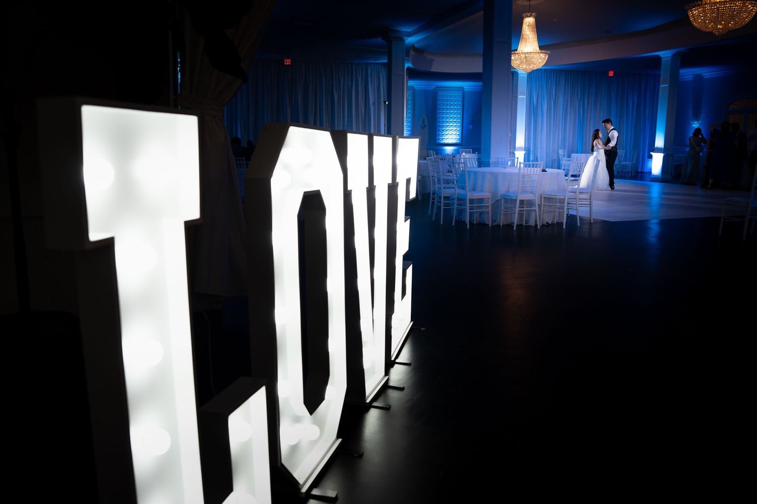 Large illuminated LOVE letters display at a blue-lit wedding reception venue.