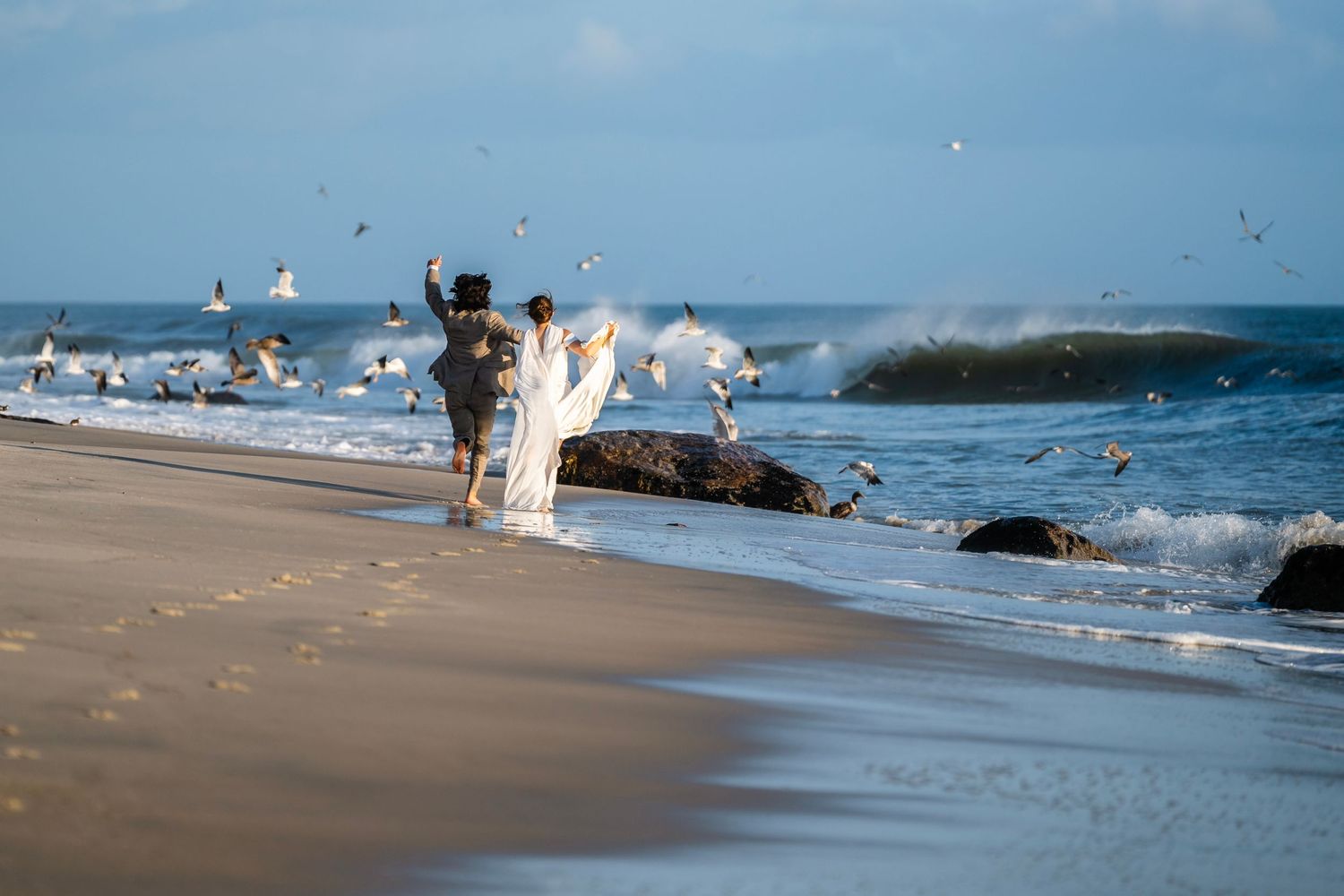 Waves crashing on a sandy beach shoreline with ocean spray in the sunlight.