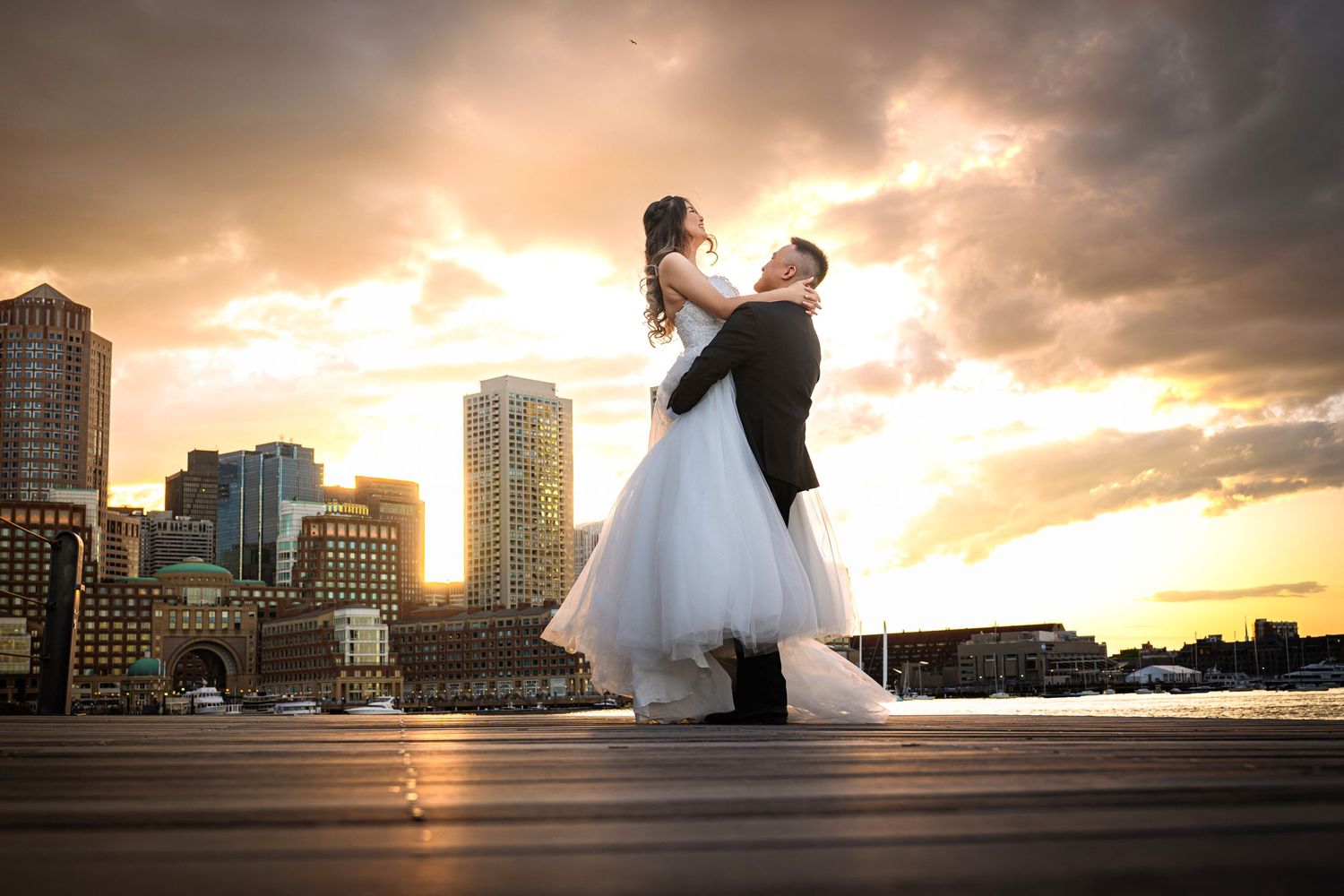 Couple dancing in a romantic embrace against a dramatic sunset cityscape with tall buildings in the background.