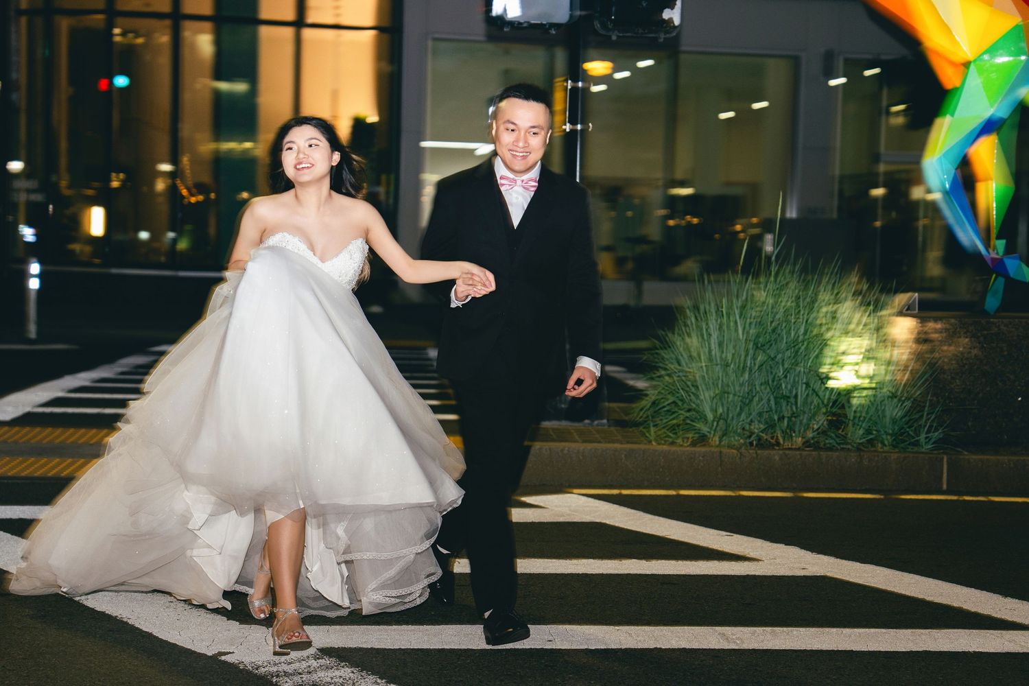 A couple runs joyfully at night in formal attire with the bride's dress flowing behind them.