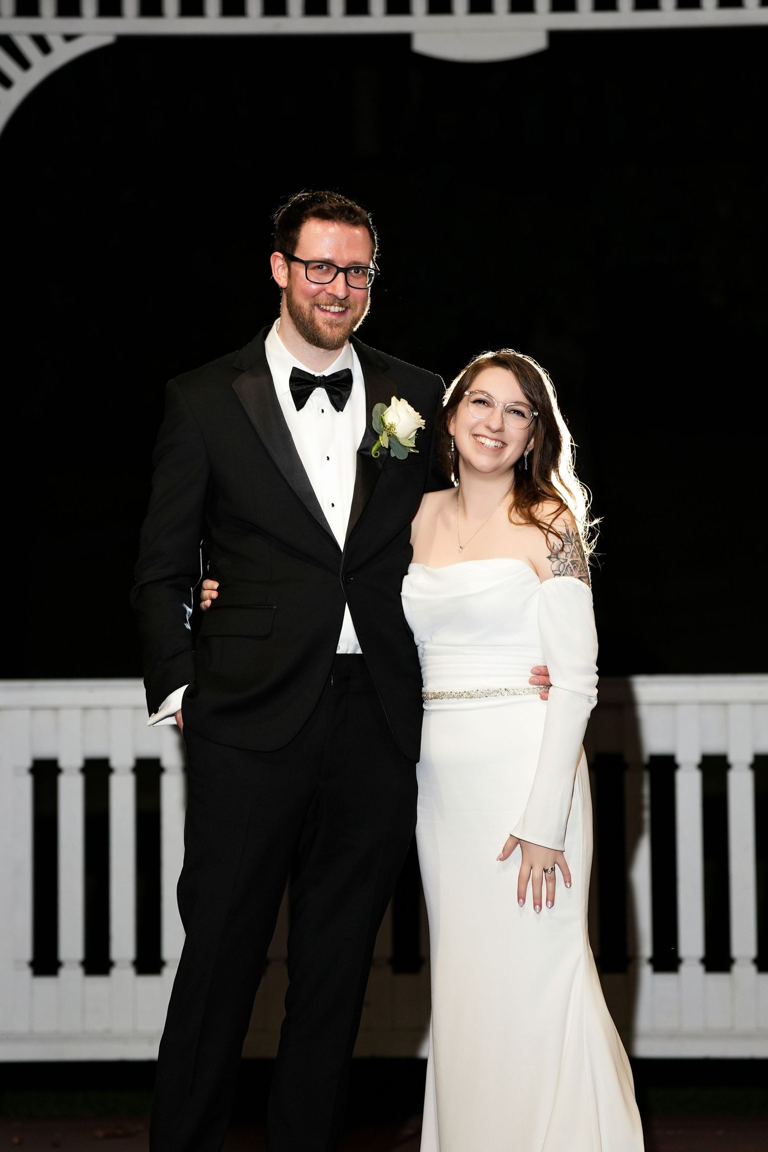 Elegant black tie wedding couple poses against dark background.