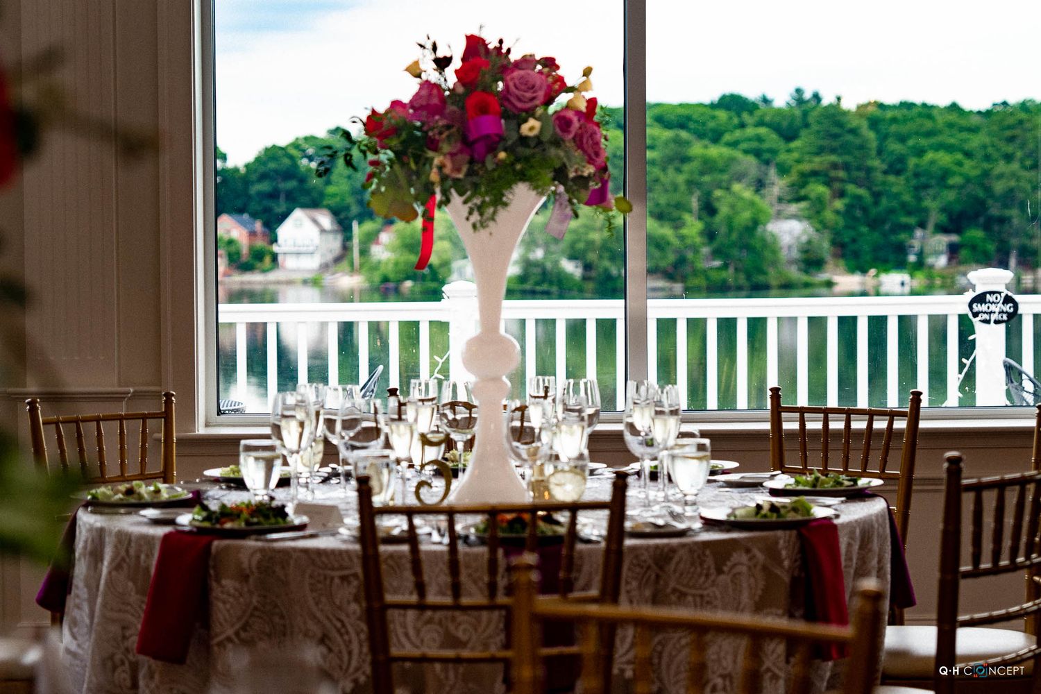 Elegant wedding reception venue with panoramic windows overlooking a scenic waterfront view and white columns.