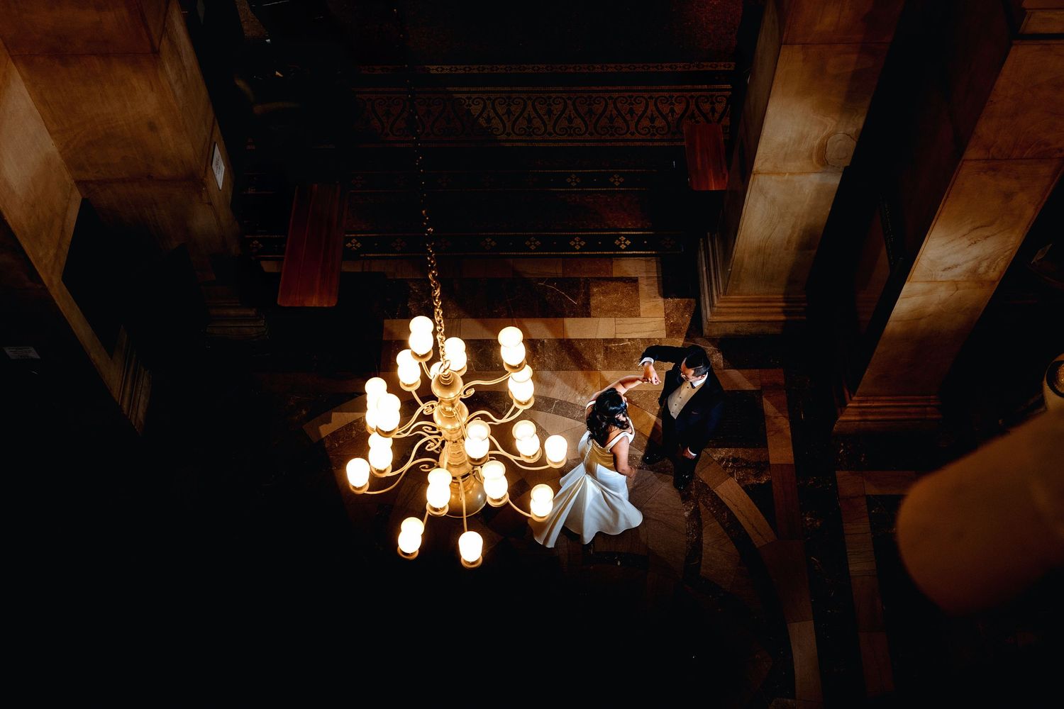 A rustic wooden barn interior with exposed beams and warm lighting from multiple chandeliers creates an elegant atmosphere.