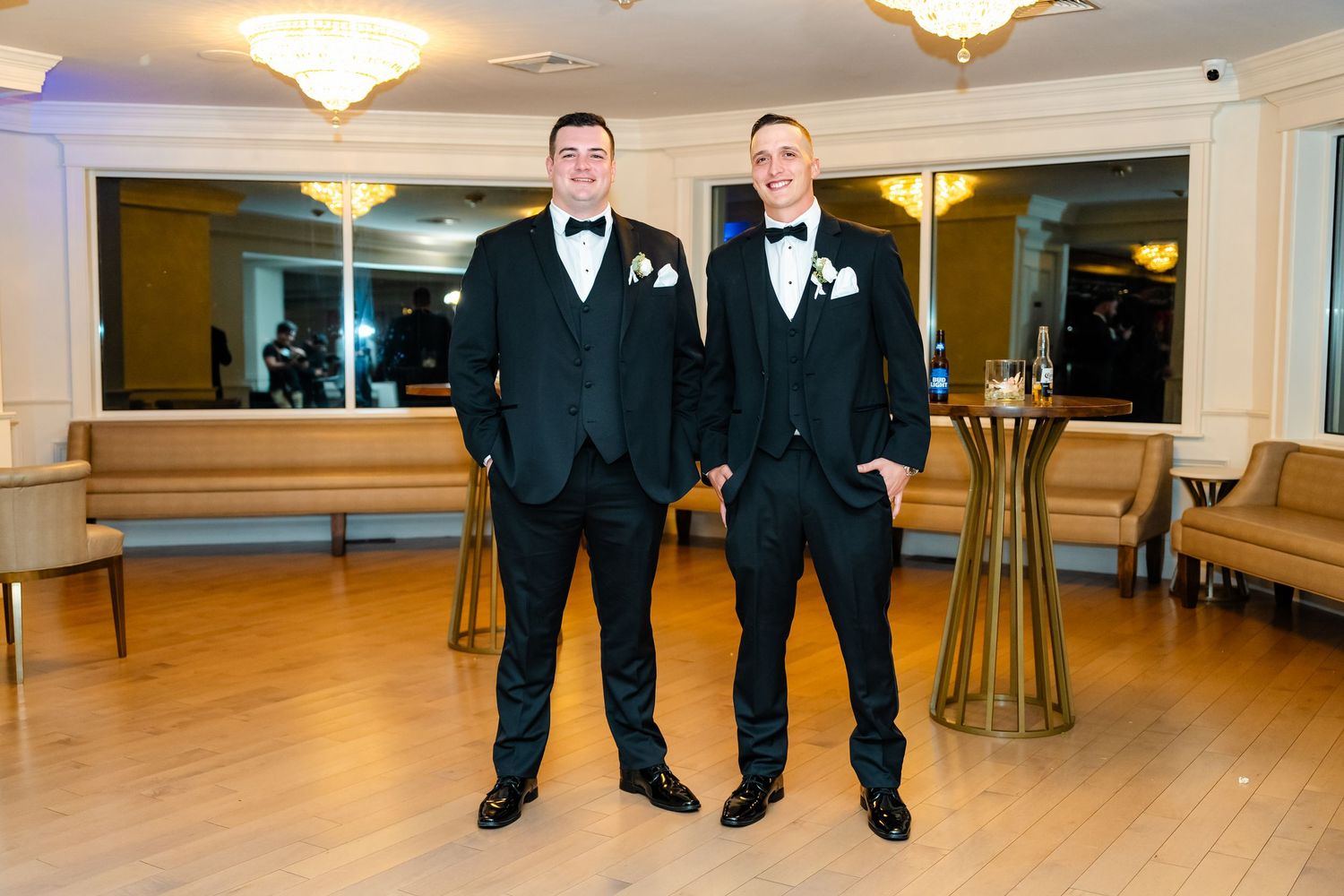 Wedding party members in formal attire stand together on a polished ballroom floor.