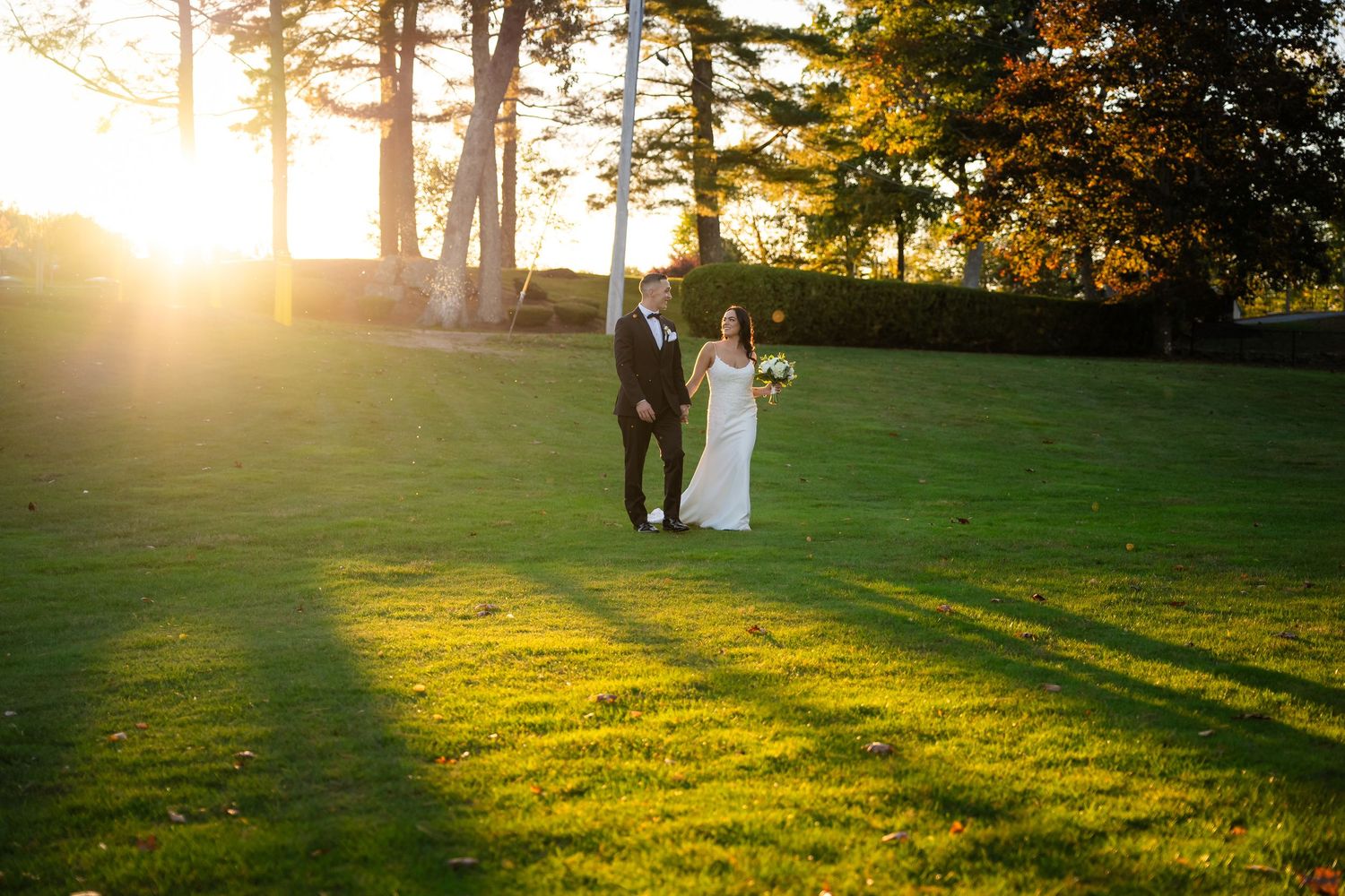 Golden sunset light streams through trees casting long shadows on a grassy hillside during an outdoor event.