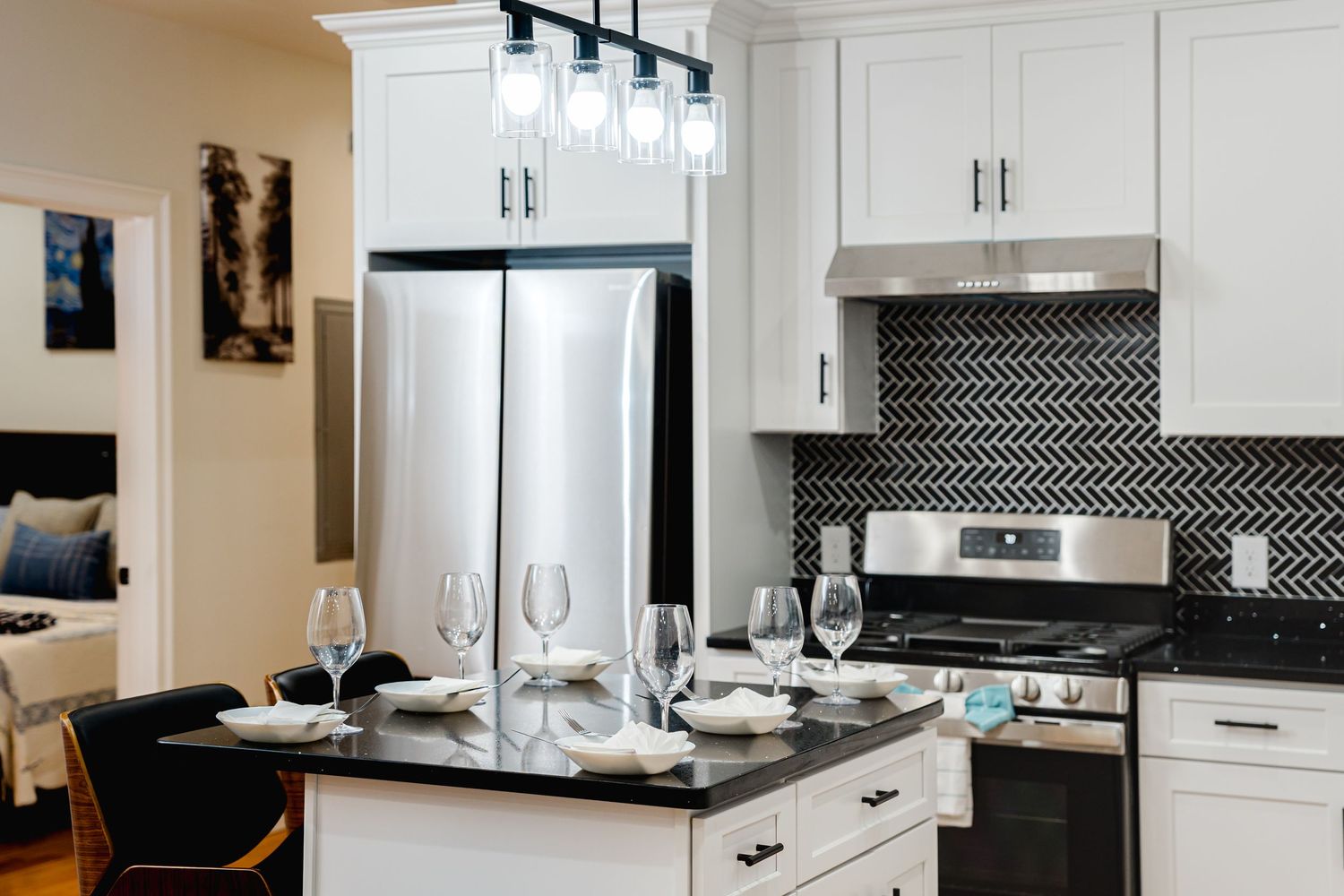 Modern white kitchen with black chevron backsplash, stainless steel appliances, and pendant lighting over white cabinets.