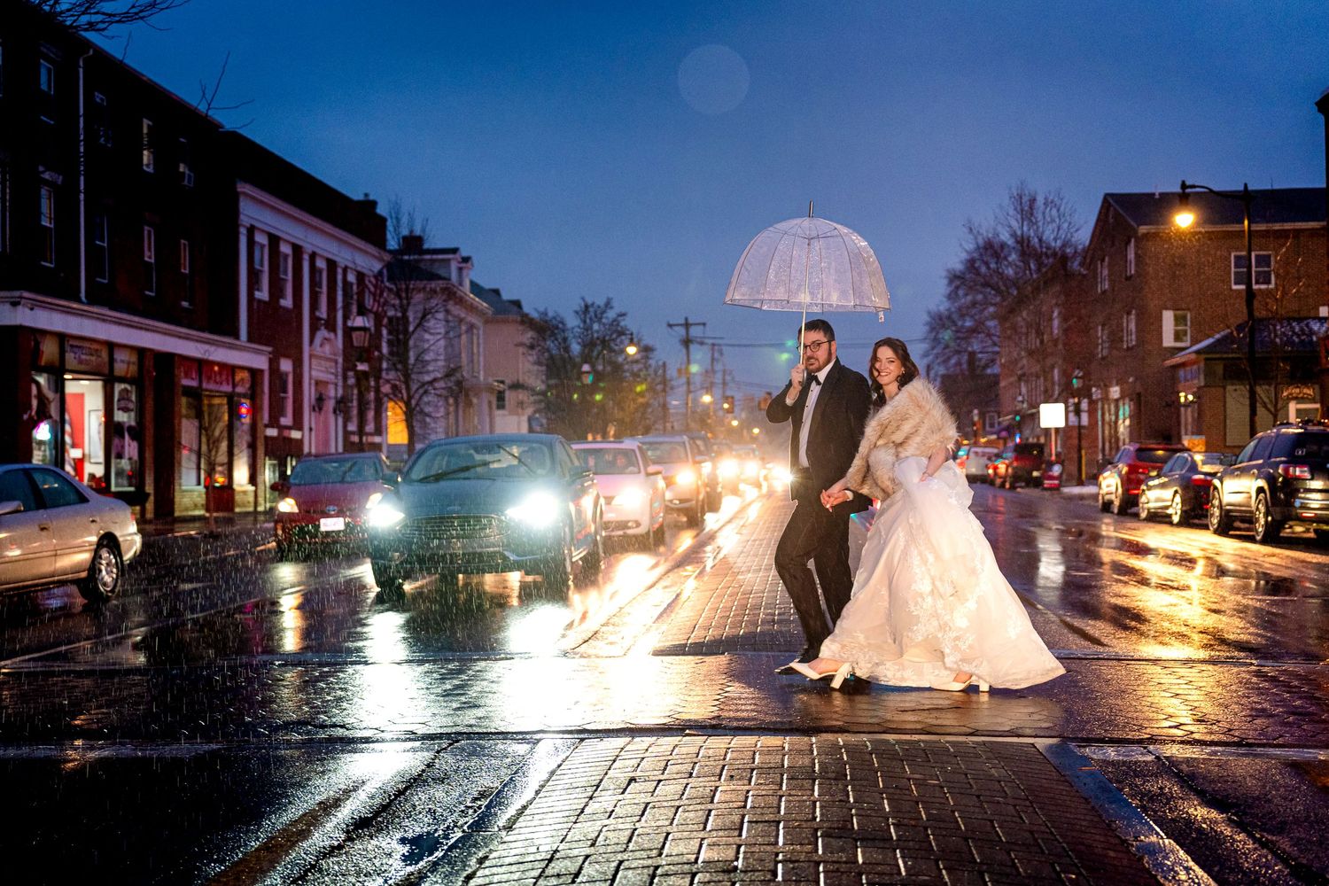 Wedding photography on wet cobblestone streets at dusk with city lights.