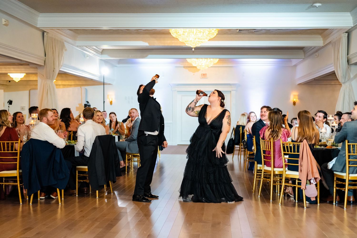 Wedding guests dance and celebrate in an elegant reception hall with gold chiavari chairs.
