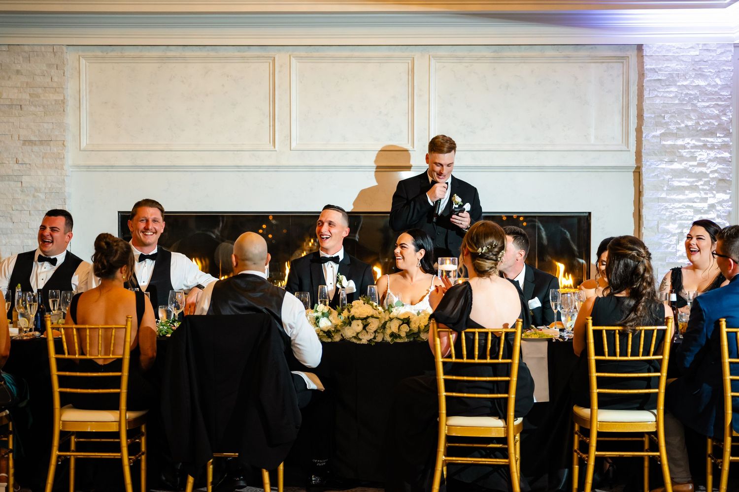 Panoramic view of wedding reception hall with guests seated at tables with gold chairs.