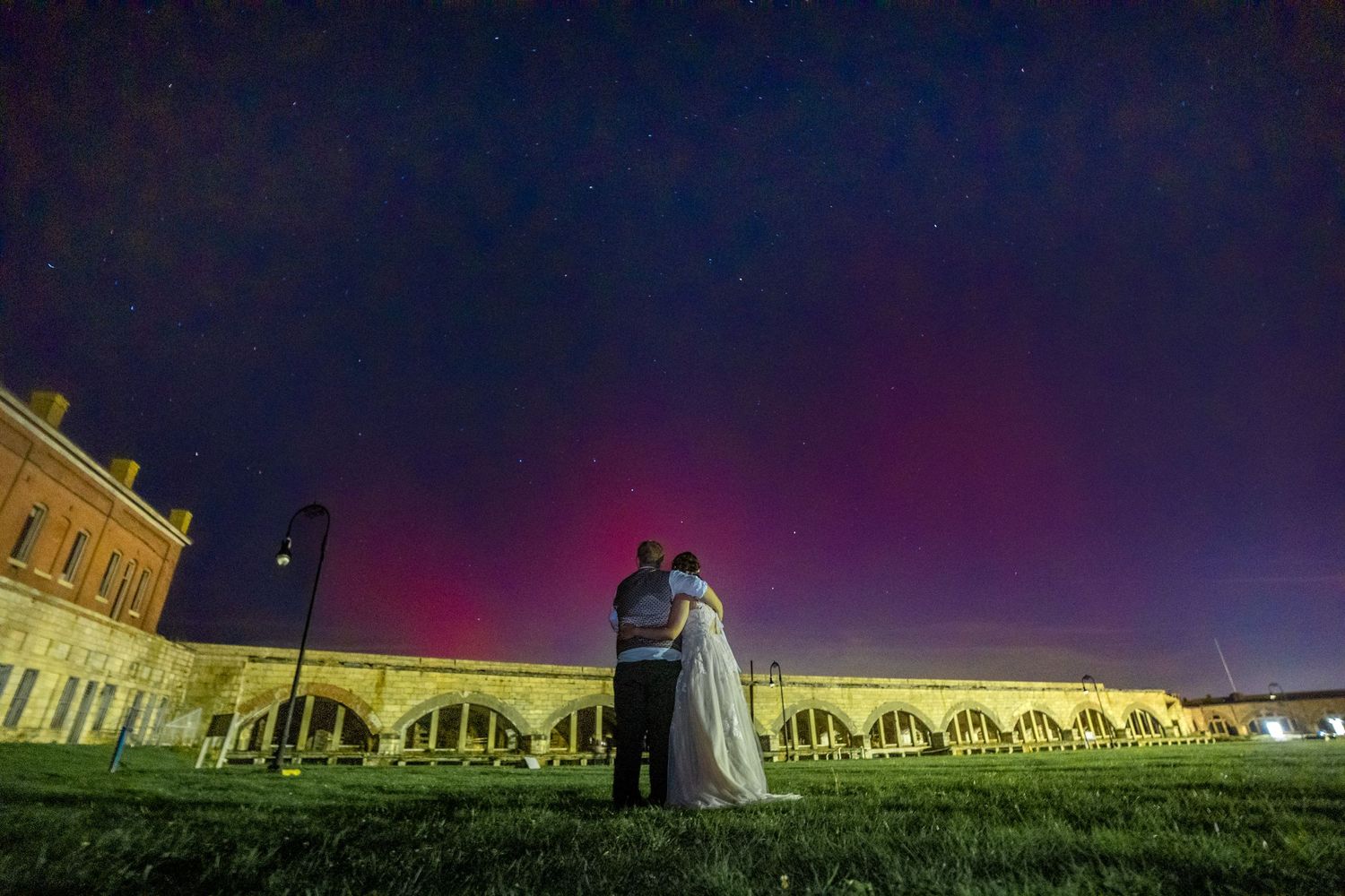 Dramatic nighttime wedding photos against illuminated historic building with purple sky.