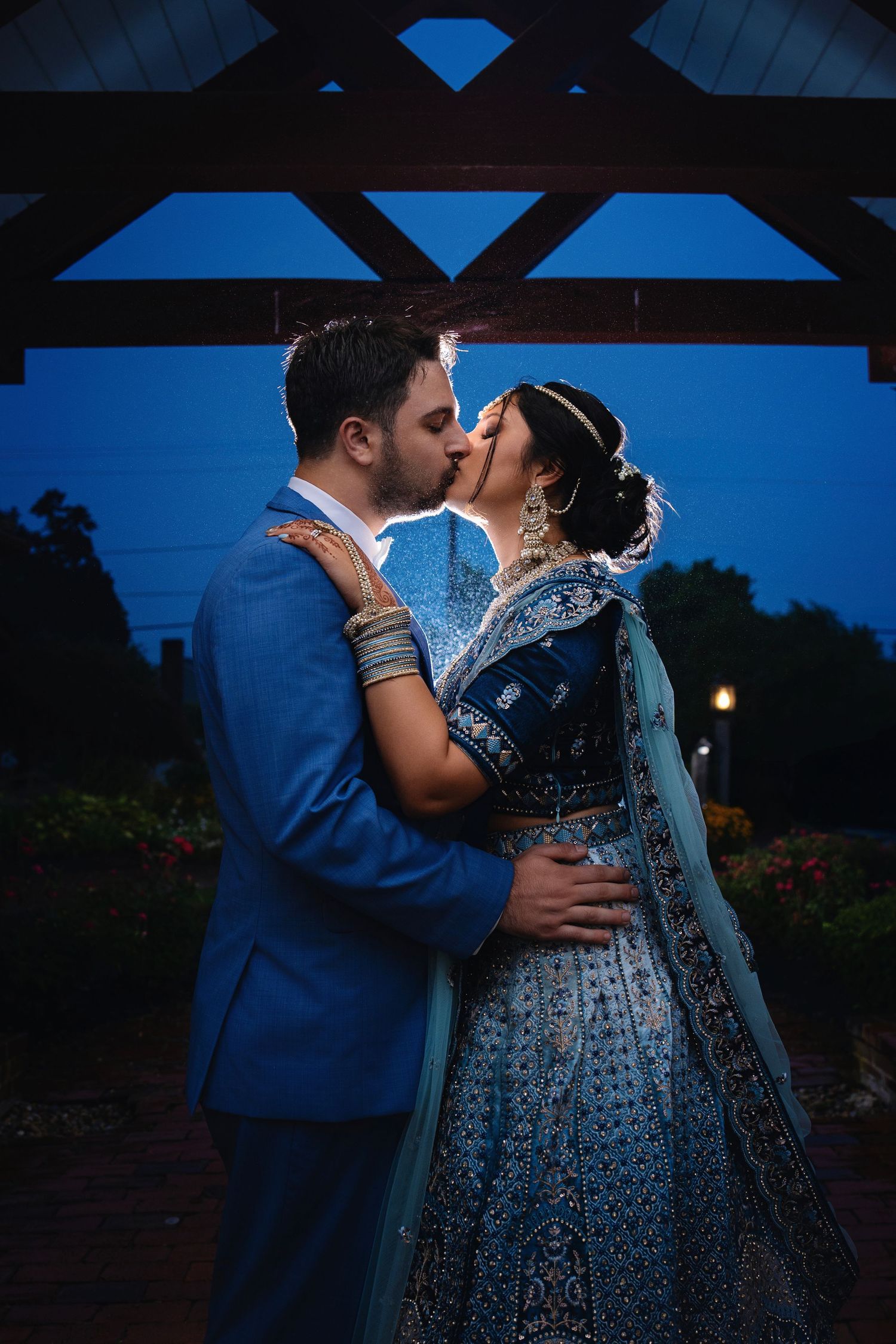 Intimate moment between couple under blue-lit architectural beams at dusk.