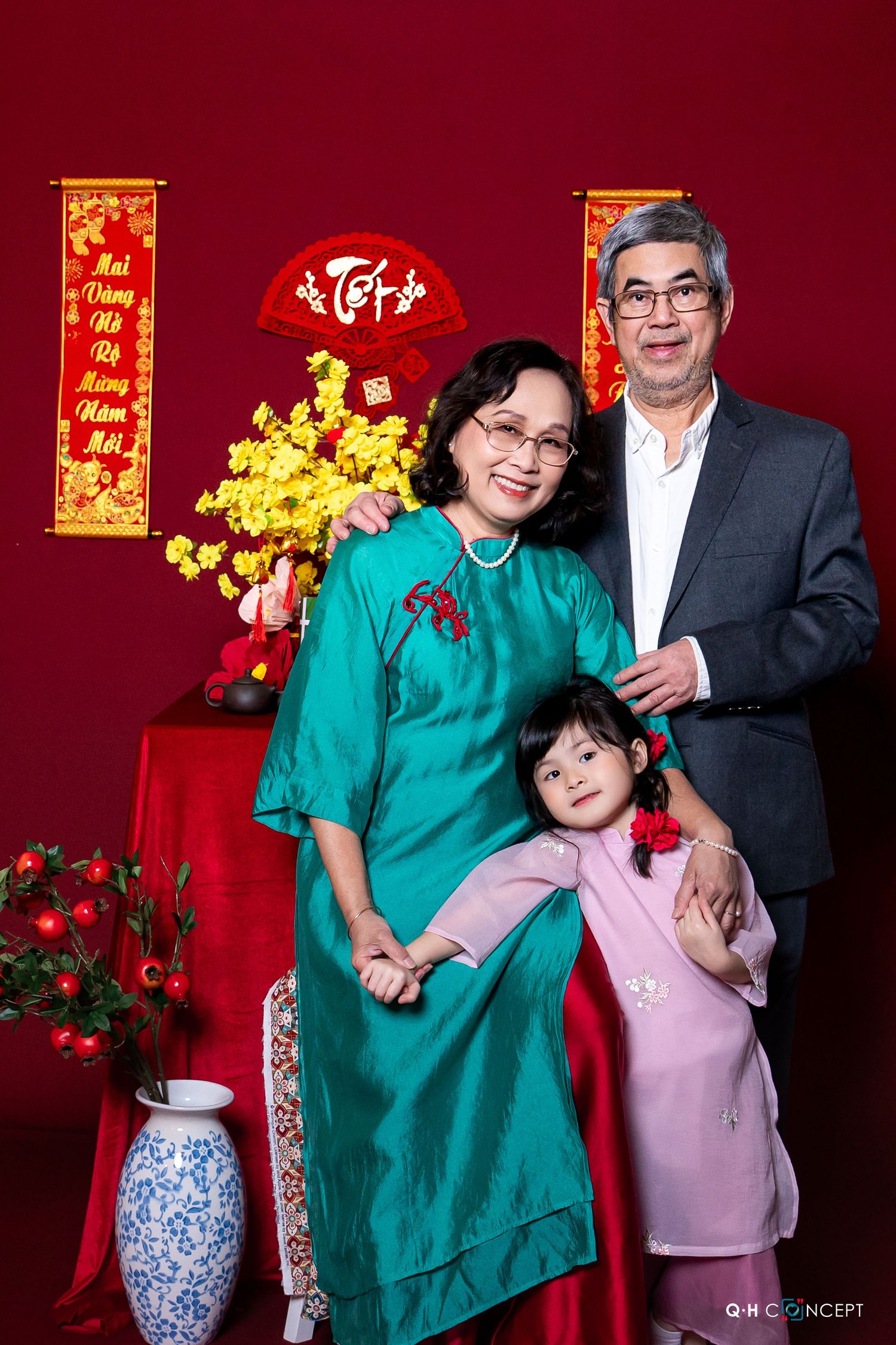 Family poses together in front of red backdrop with traditional Chinese New Year decorations and golden ornaments.