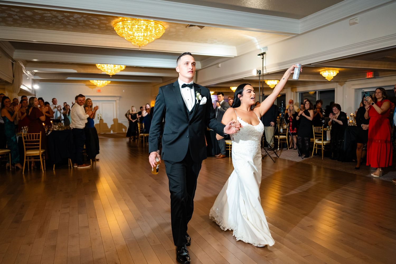 Newlyweds make grand entrance into reception ballroom with guests cheering.