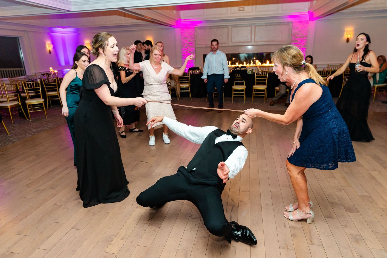 Wedding guests dancing energetically on a wooden dance floor with colorful purple lighting.