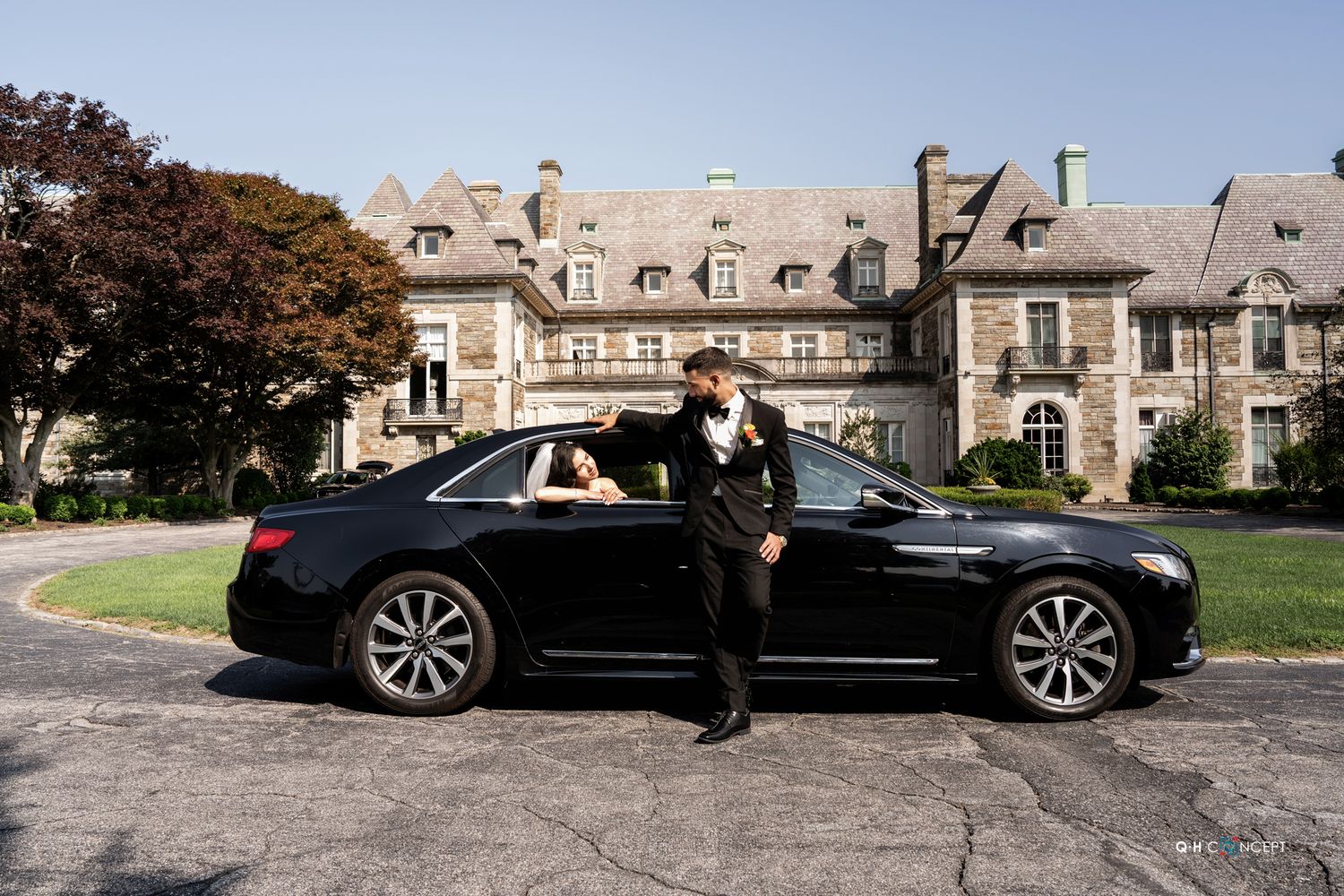 A series of black luxury vehicles parked in front of a grand stone mansion with classic architecture.