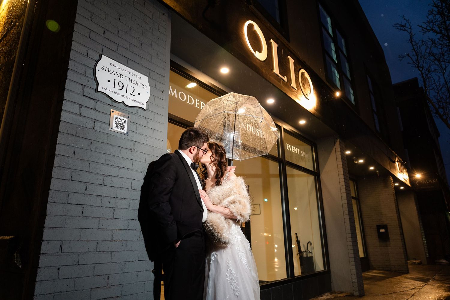 Romantic nighttime wedding portrait outside a storefront with glowing signage.