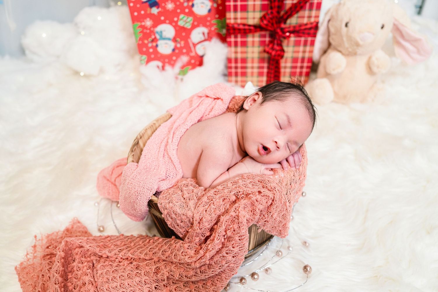 A peaceful newborn wrapped in a pink blanket surrounded by Christmas decorations.