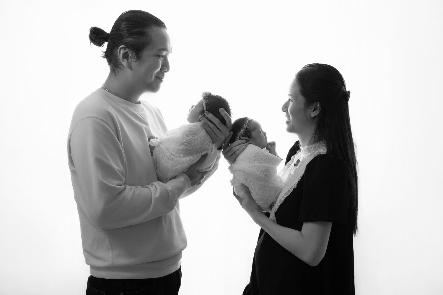Black and white portrait of parents holding newborn baby against white background.