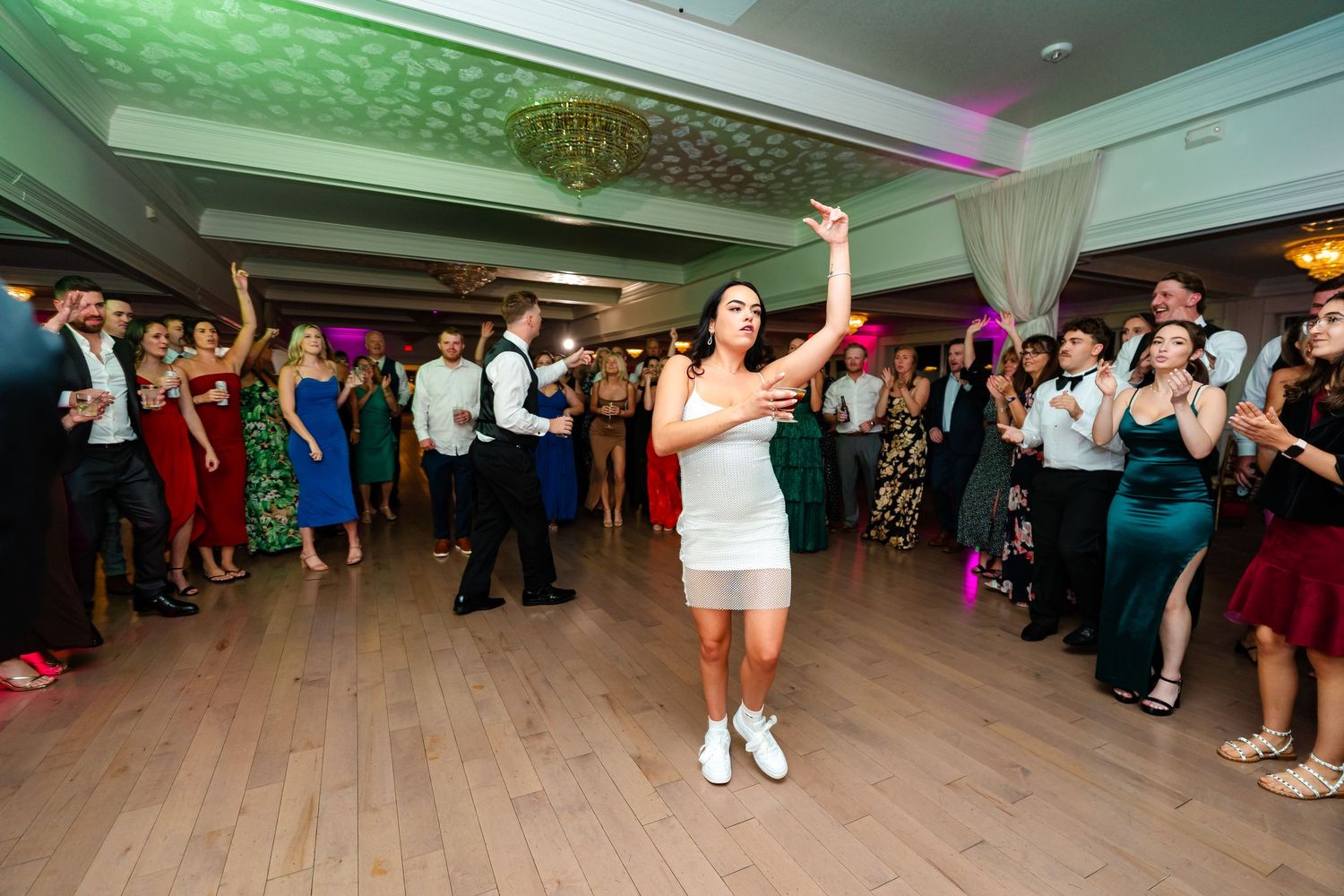 Wedding reception dance floor filled with guests celebrating under green ambient lighting.