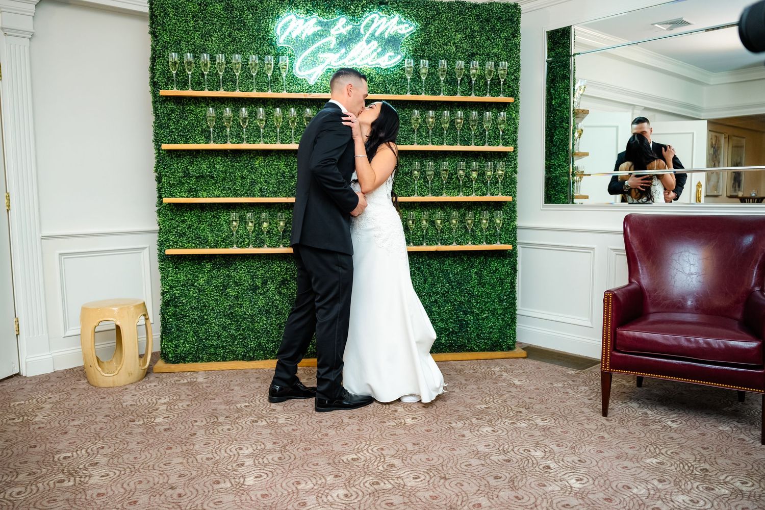 Couple shares romantic moment in front of decorative green wall with champagne glass display.