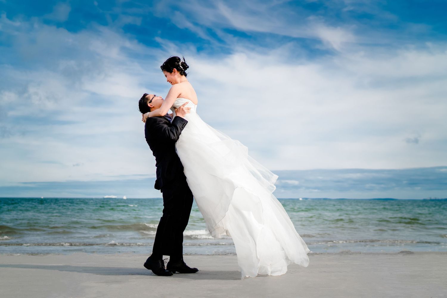 Romantic beach wedding photoshoot with flowing white dress against ocean backdrop.