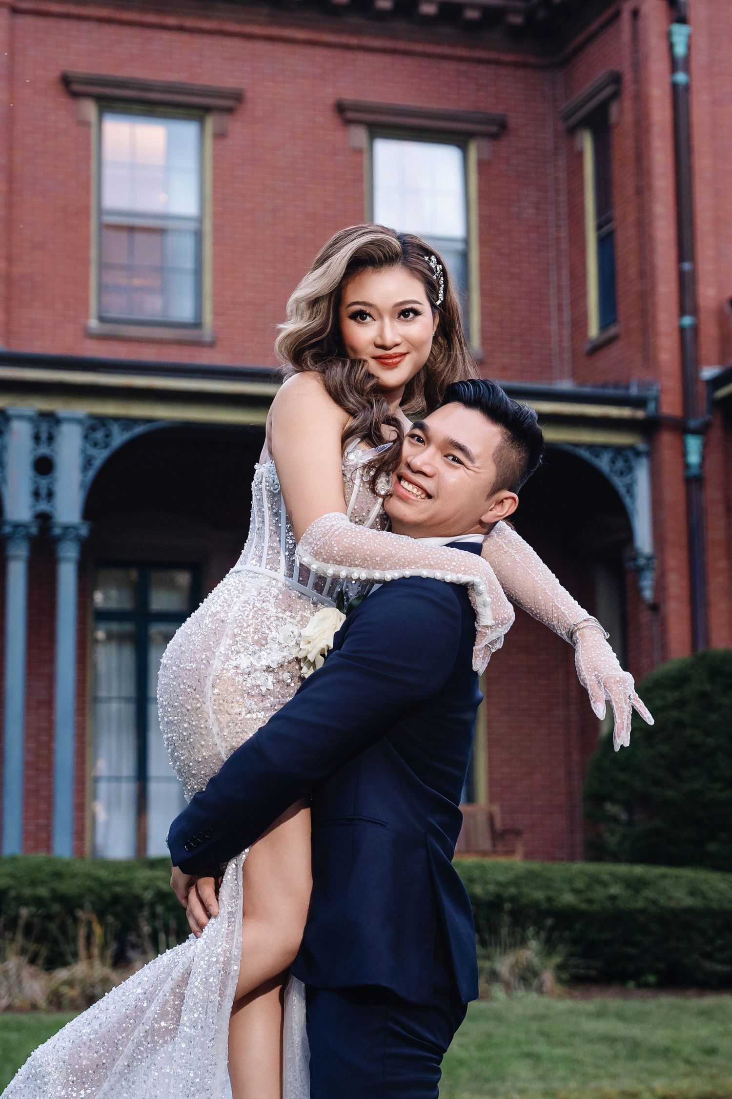 A romantic wedding couple poses playfully outside a historic brick building.