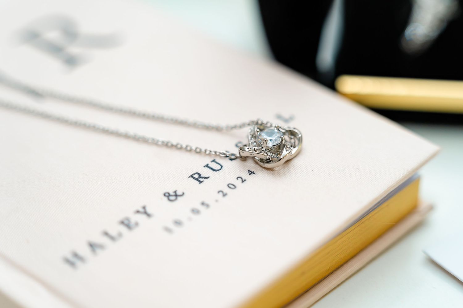 A delicate engagement ring with aqua stone rests on a white and gold wedding invitation.