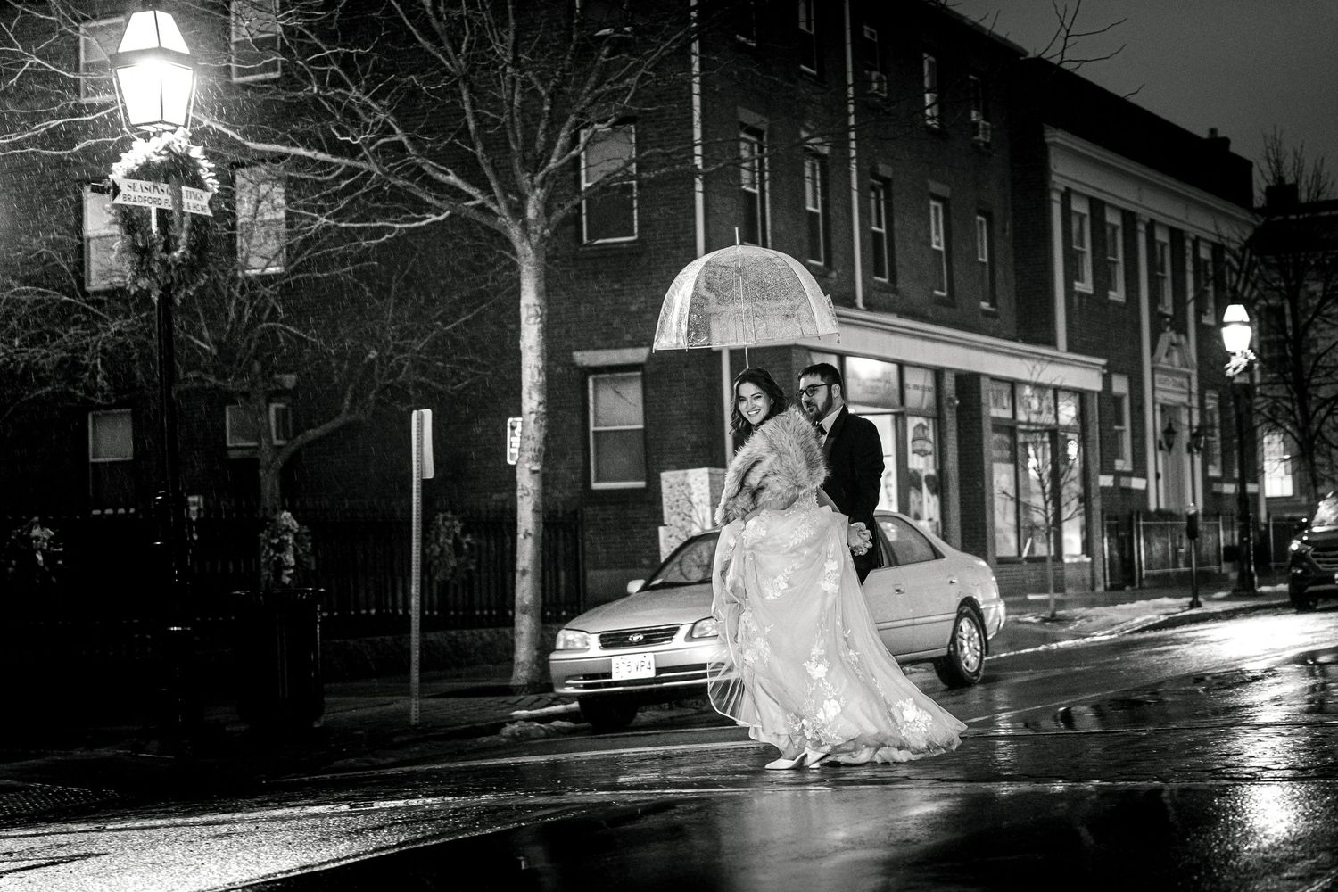 Black and white nighttime wedding photography on a rain-soaked urban street.