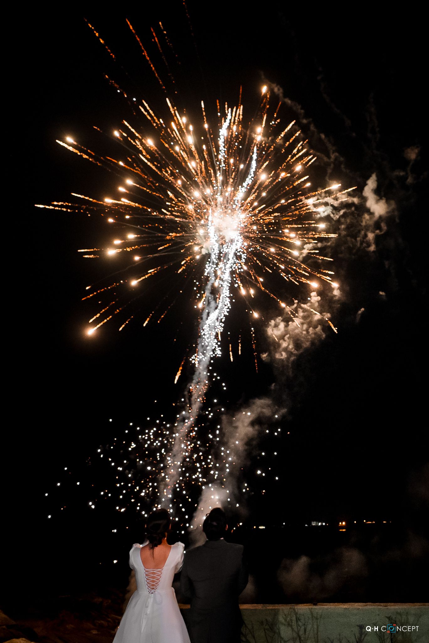 A dramatic firework display illuminates a couple during their wedding celebration.