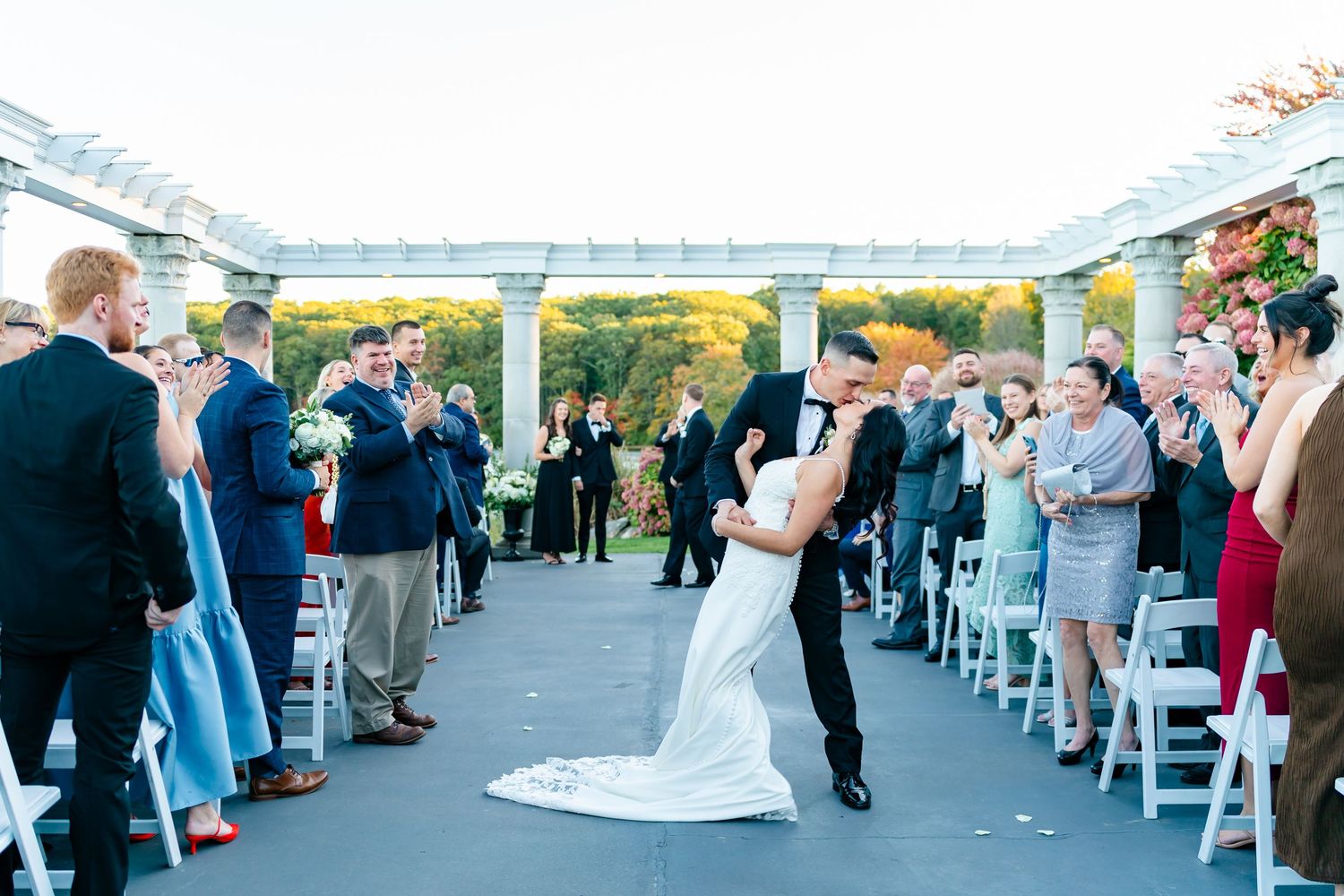Wedding ceremony guests stand in anticipation as couple exchanges vows on an outdoor terrace overlooking scenic views.