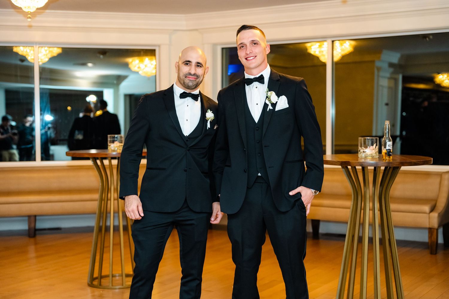 Groomsmen in black tuxedos pose together in an elegant ballroom setting.