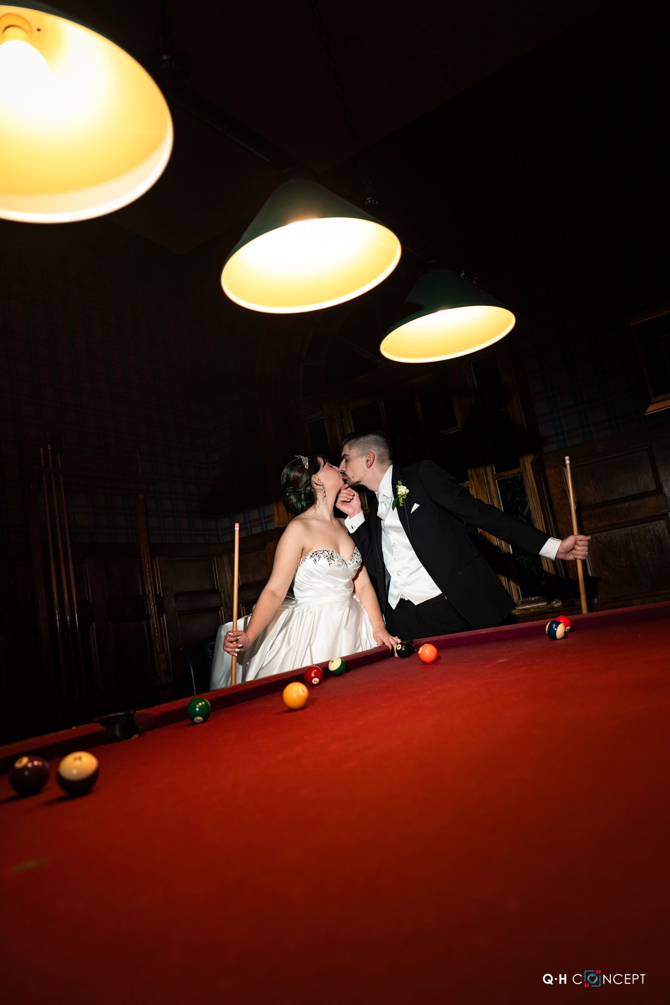 A playful wedding scene on a pool table with dramatic overhead lighting creating unique shadows.