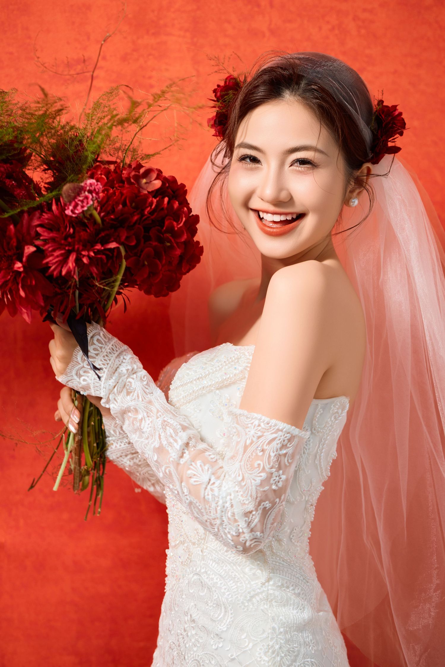 A bridal portrait against a vibrant red wall with deep red floral bouquet.