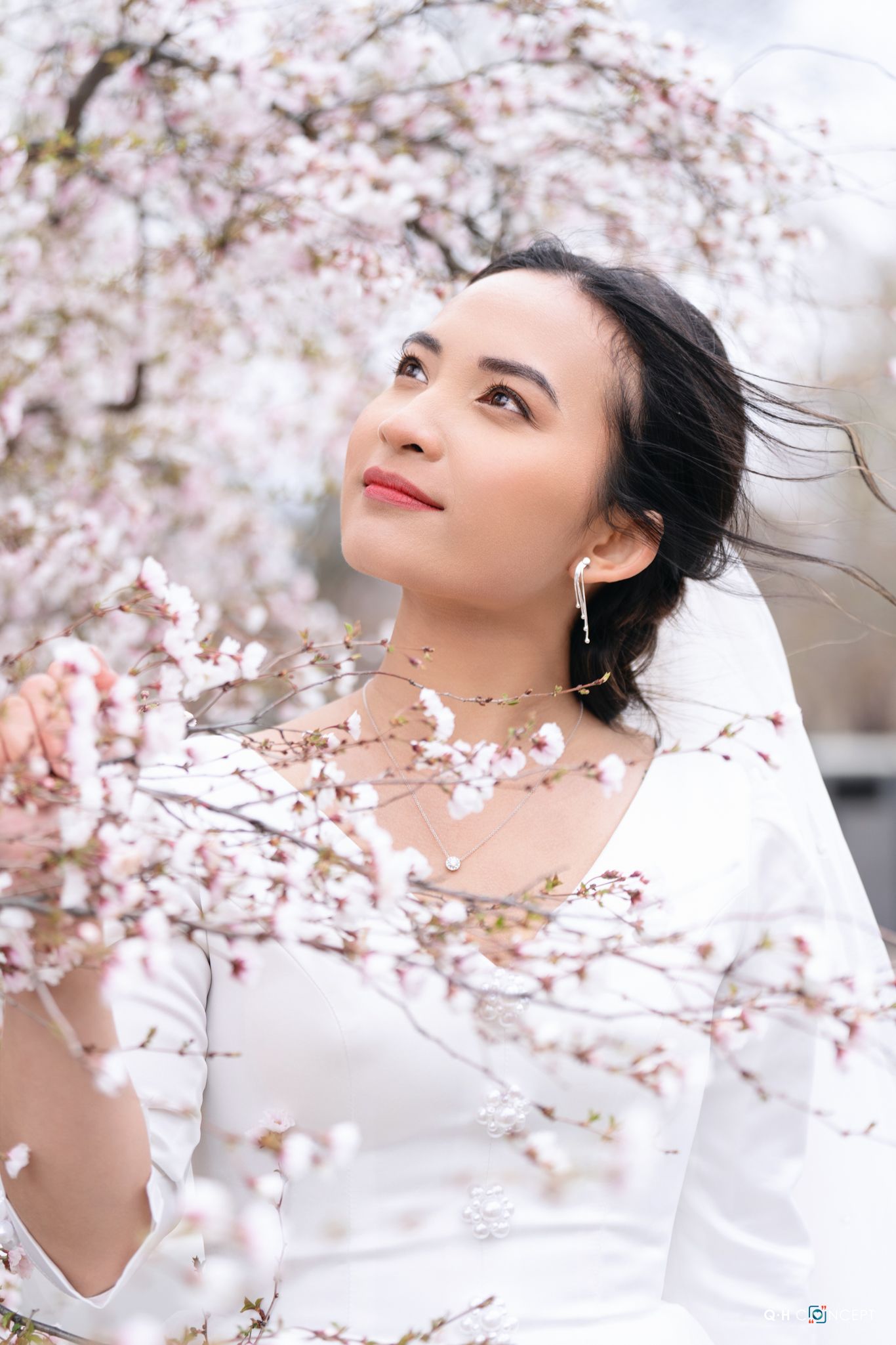 Ethereal spring portrait amidst delicate cherry blossoms with soft white fabric creating a dreamy atmosphere.