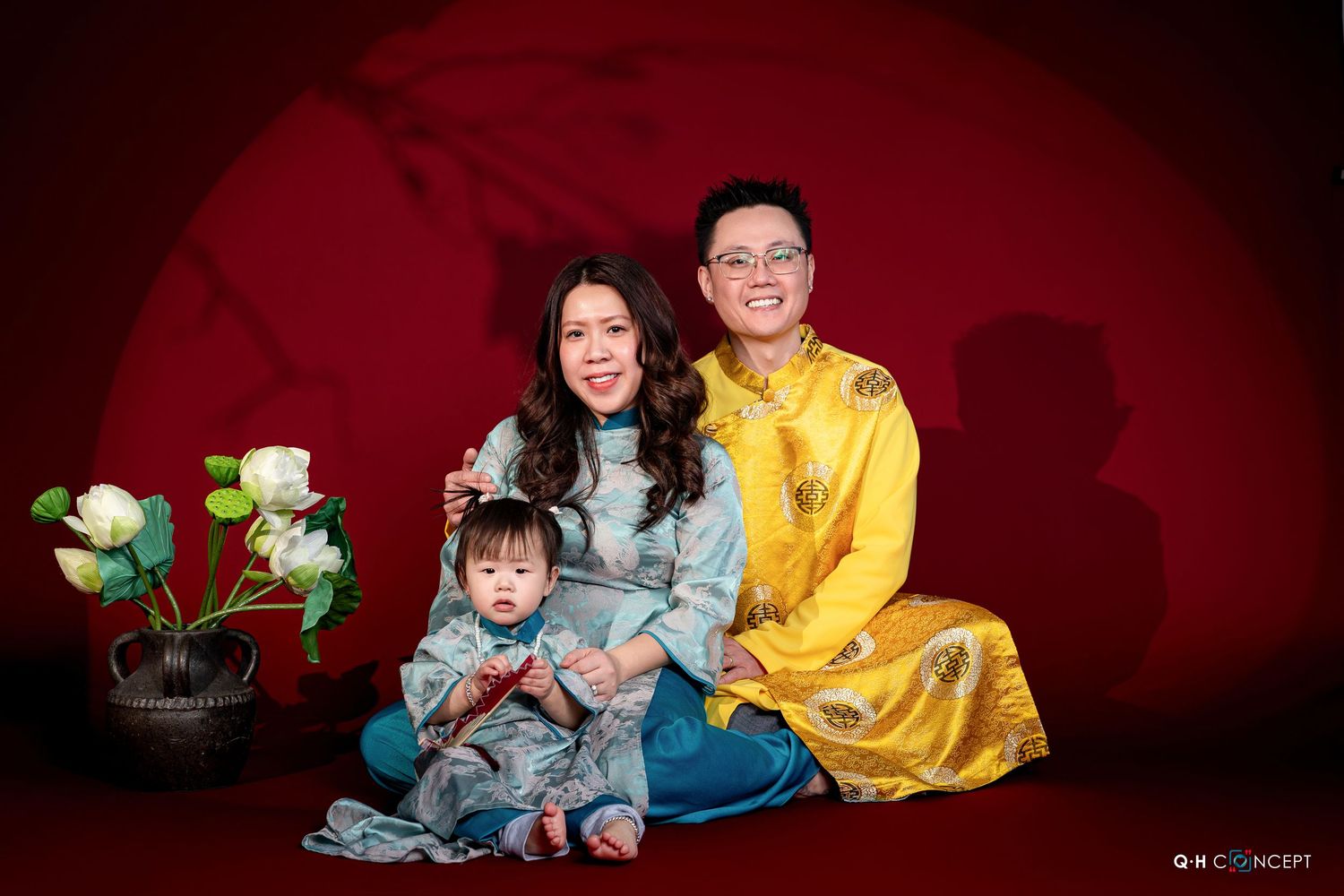 Family wearing blue and yellow outfits poses for professional portraits against dark red backdrop in studio setting.