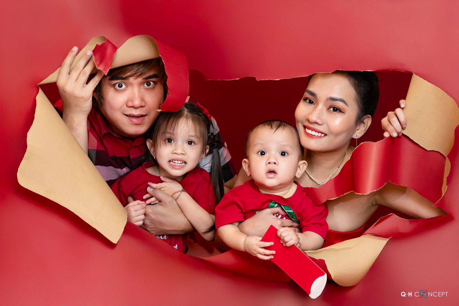 A family poses together through torn red paper background for a festive holiday portrait.
