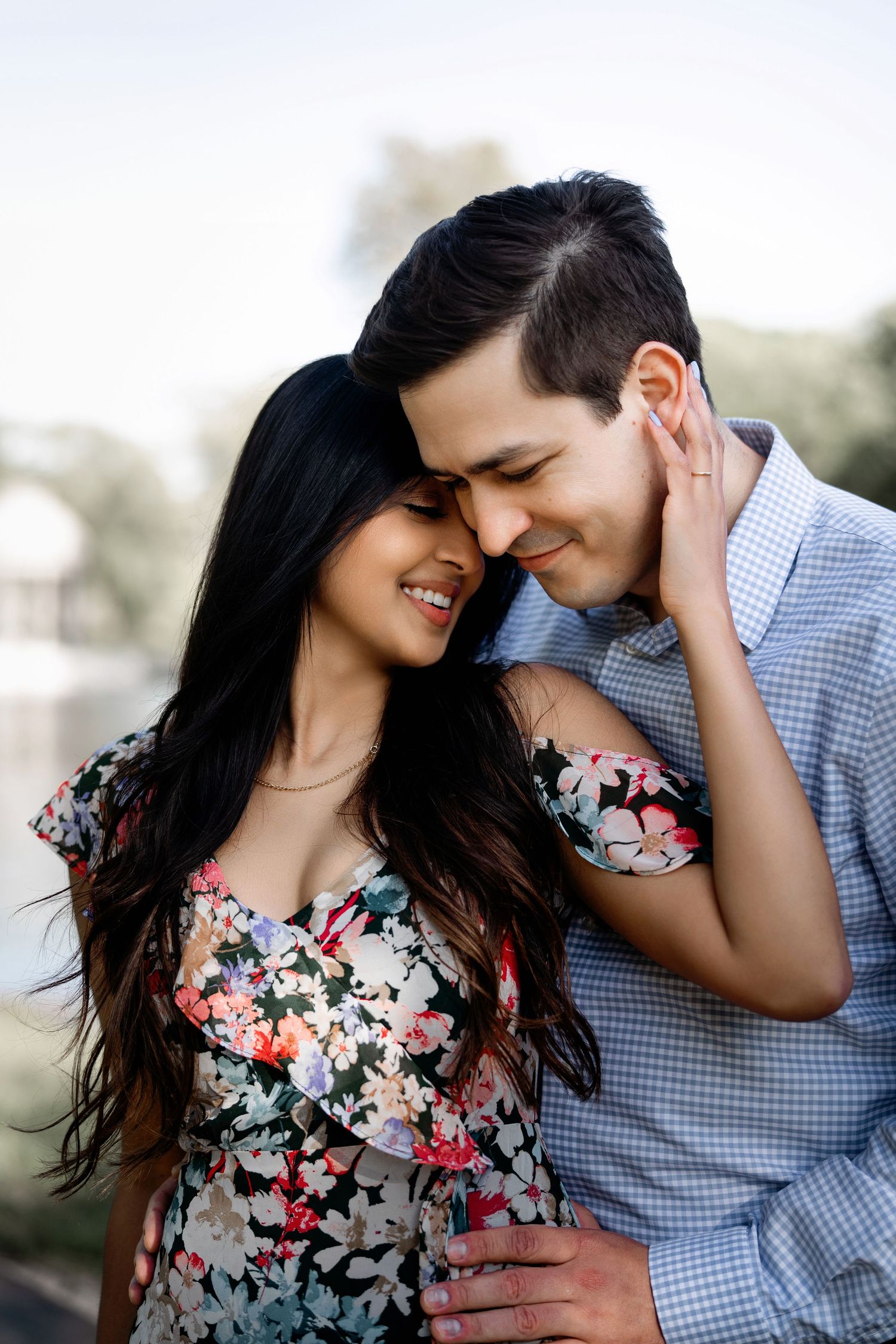 Couple in floral dress and checkered shirt share intimate moment during engagement shoot.